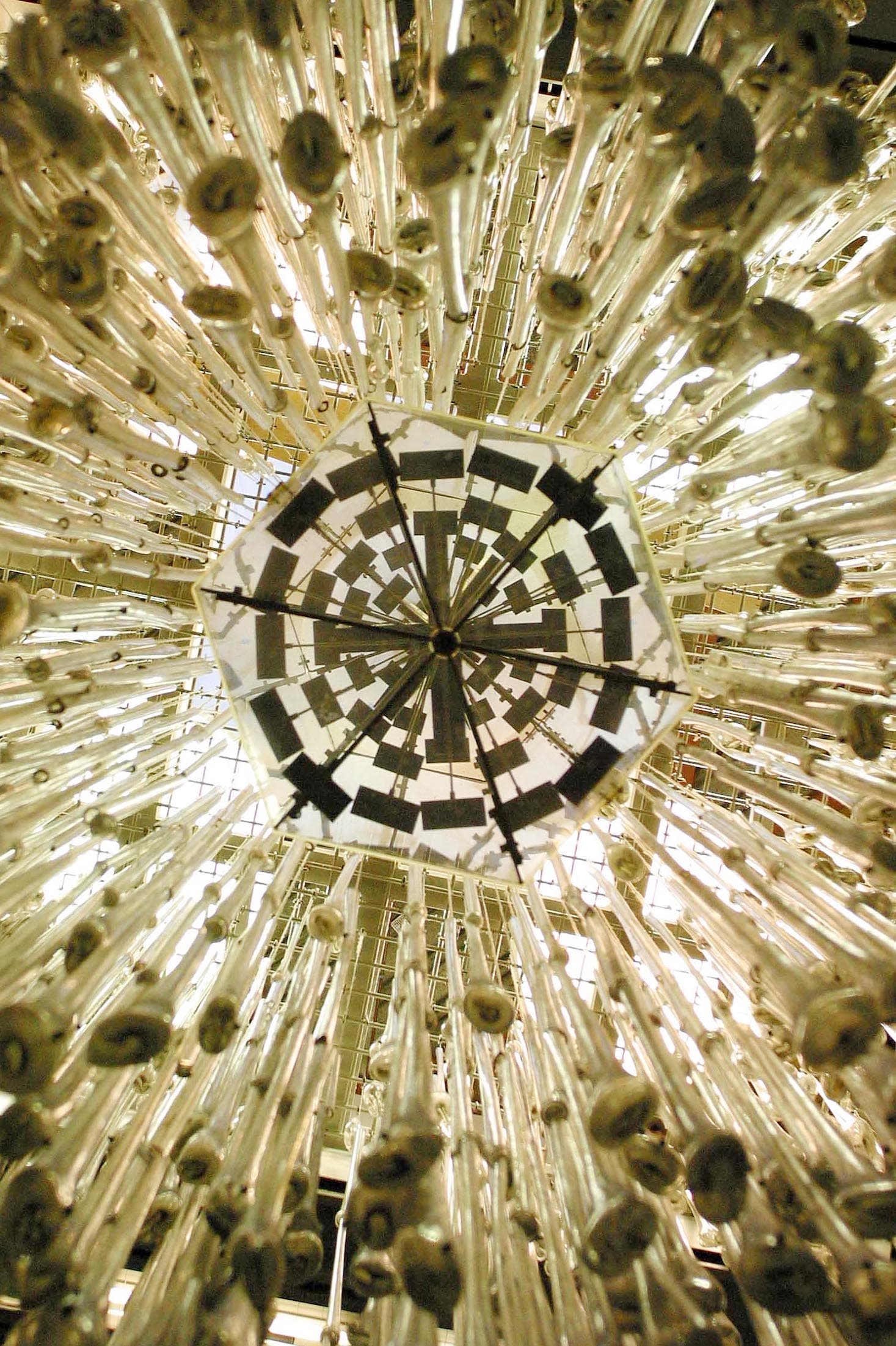 Looking up at a chandelier with numerous hanging glass tubes and a geometric, mirrored centrepiece.