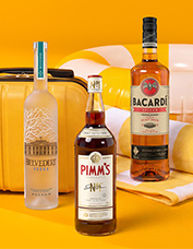 Three liquor bottles—Belvedere Vodka, Pimm's, and Bacardi—are displayed against a bright yellow background with a suitcase and beach ball.