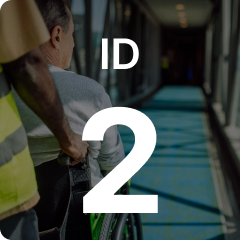 Person pushing a man in a wheelchair down a well-lit hallway, with "ID 2" prominently displayed over the image.