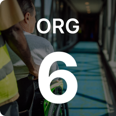 A person pushes another in a wheelchair down a well-lit corridor with "ORG 6" overlaid on the image.