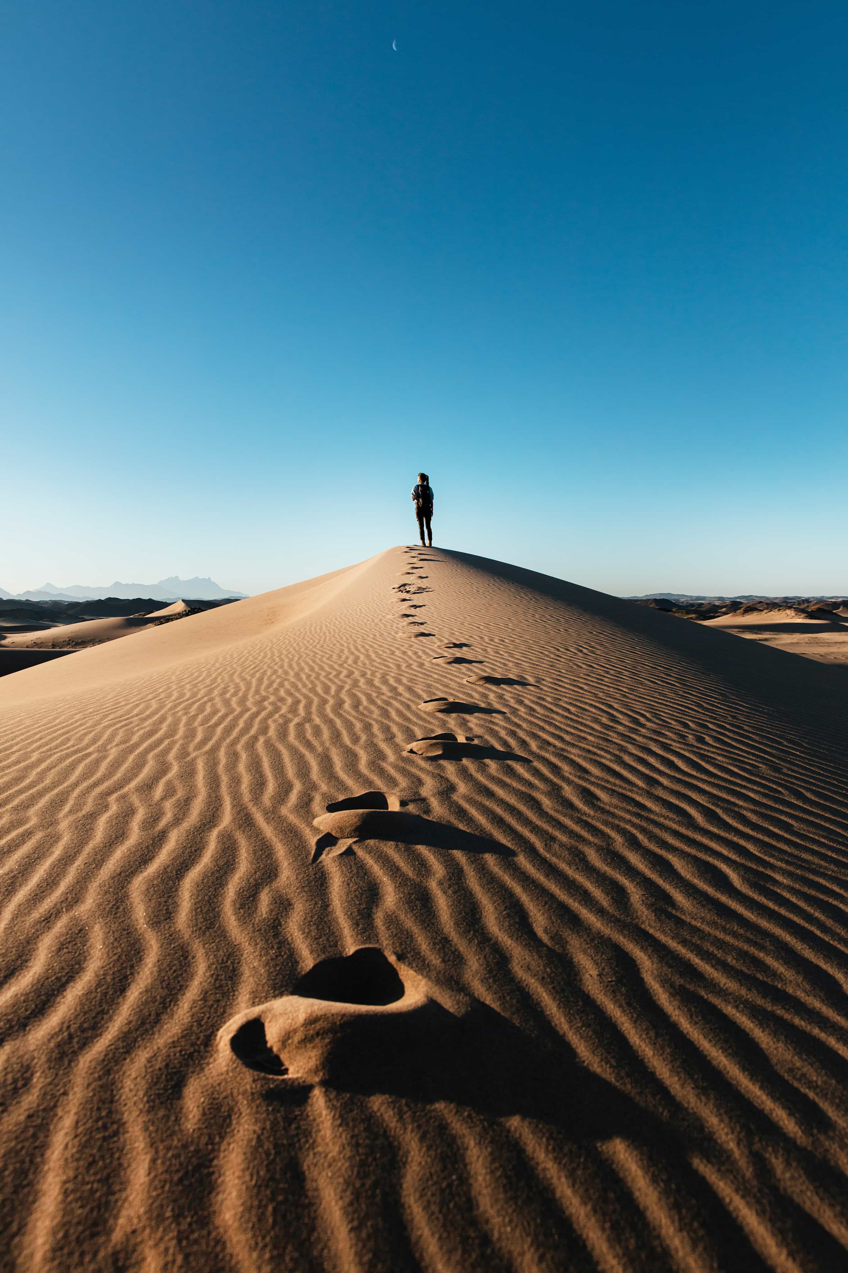 Person stood on top of hill in desert with footsteps following