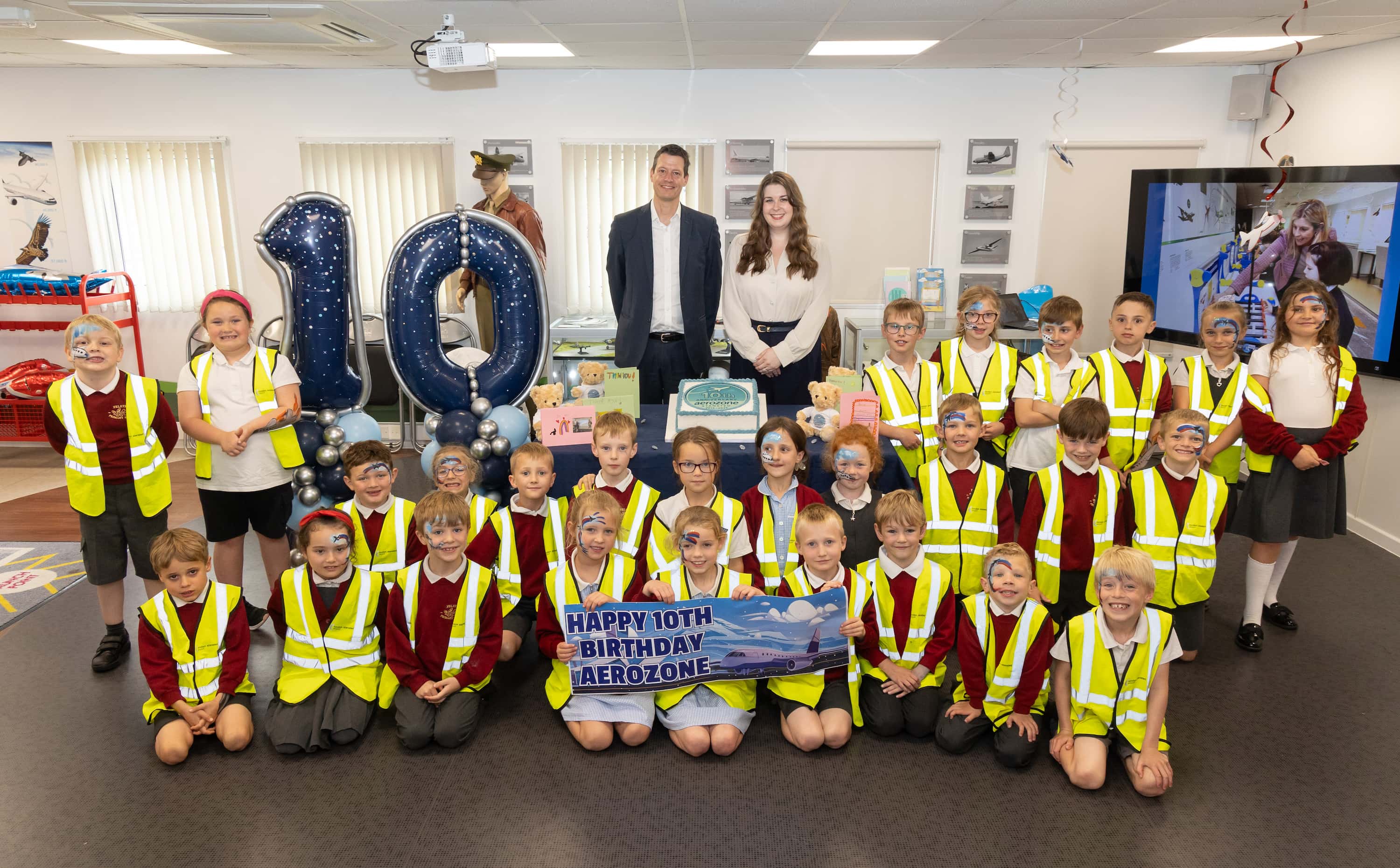 a group of young school children sat on the floor with the number '20,000' in large blue helium balloons behind them
