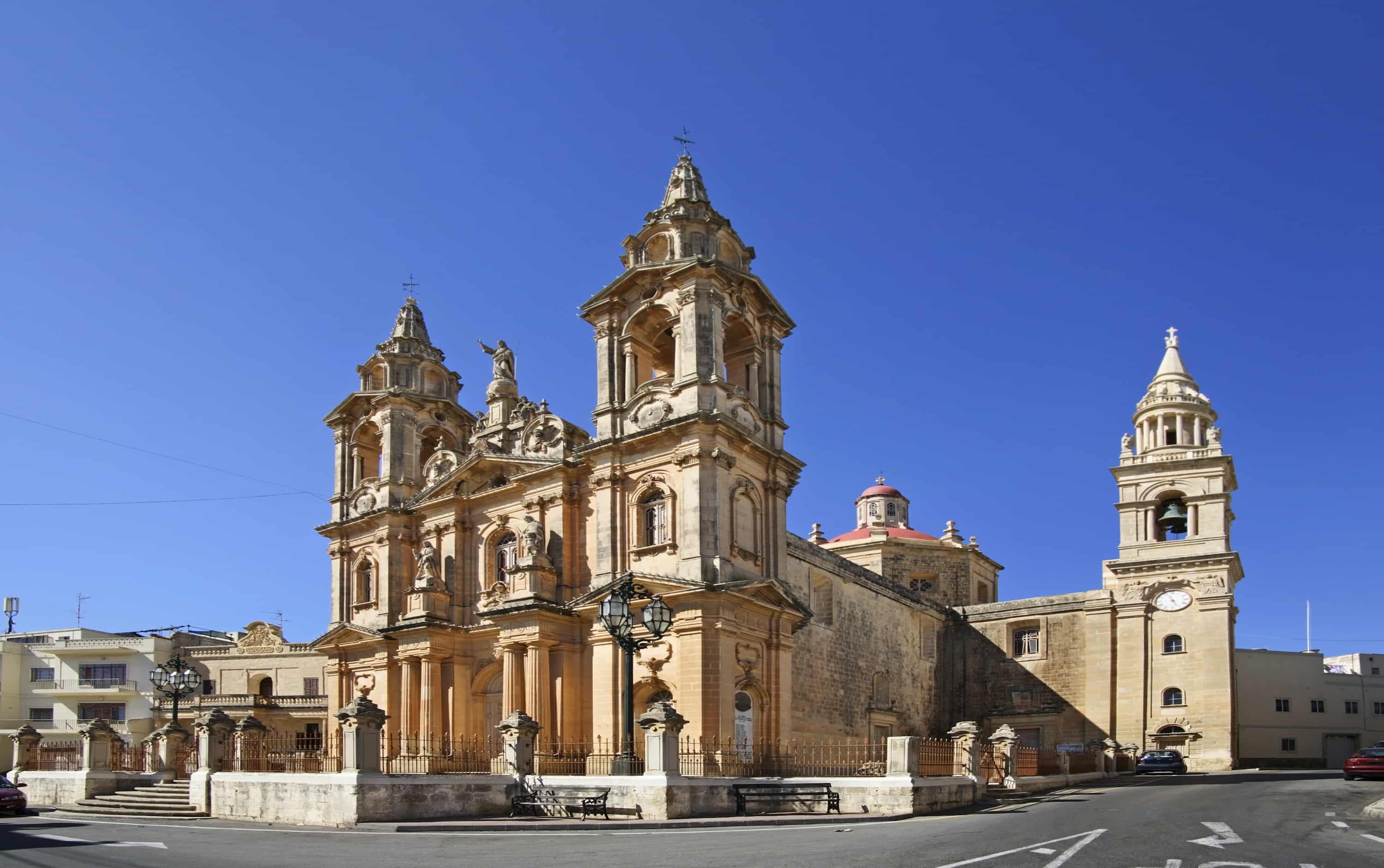 Historic church with ornate architecture, twin bell towers, and a central dome, set against a clear blue sky.