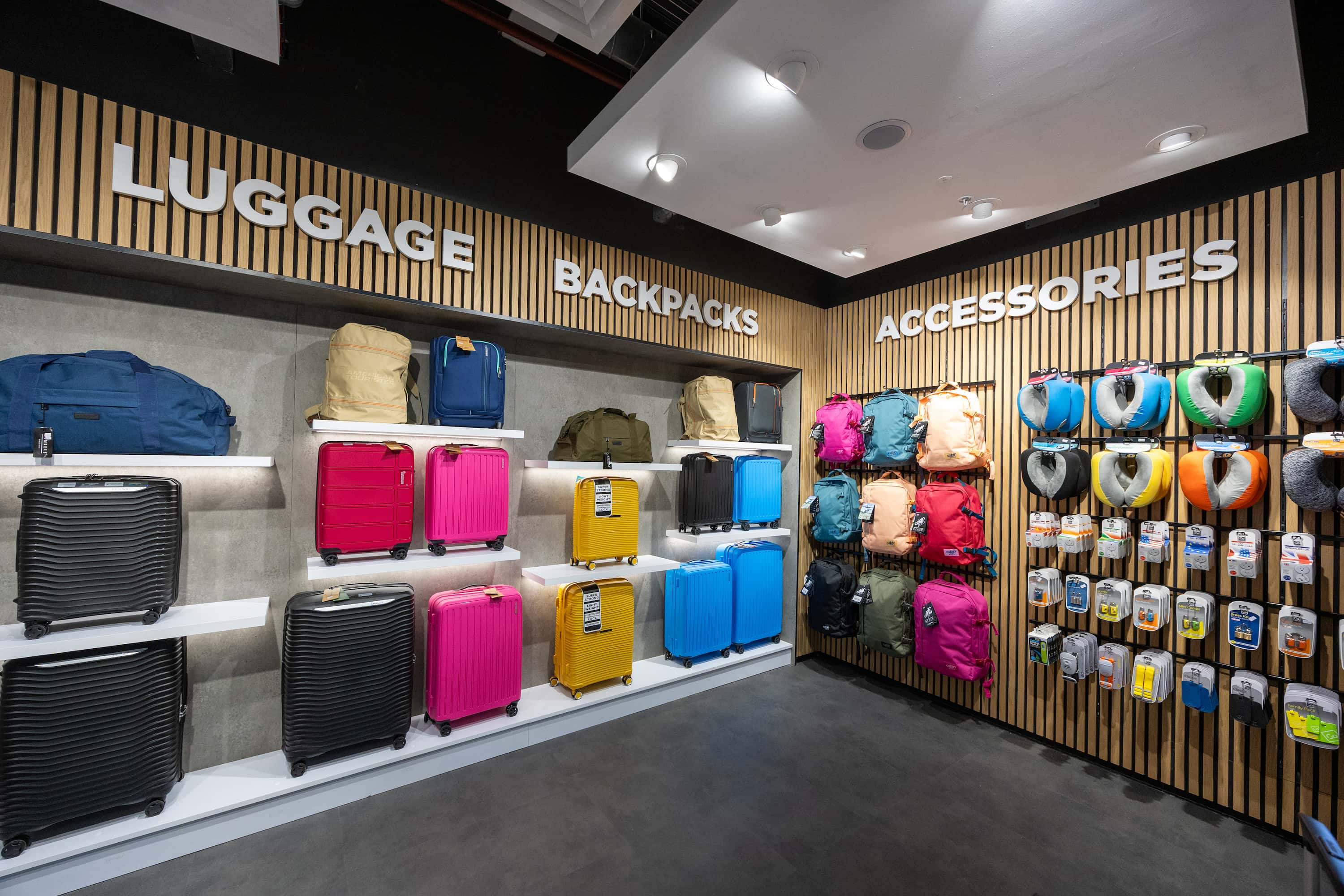 Luggage store display with colourful suitcases, backpacks, and travel accessories on wooden walls and shelves.