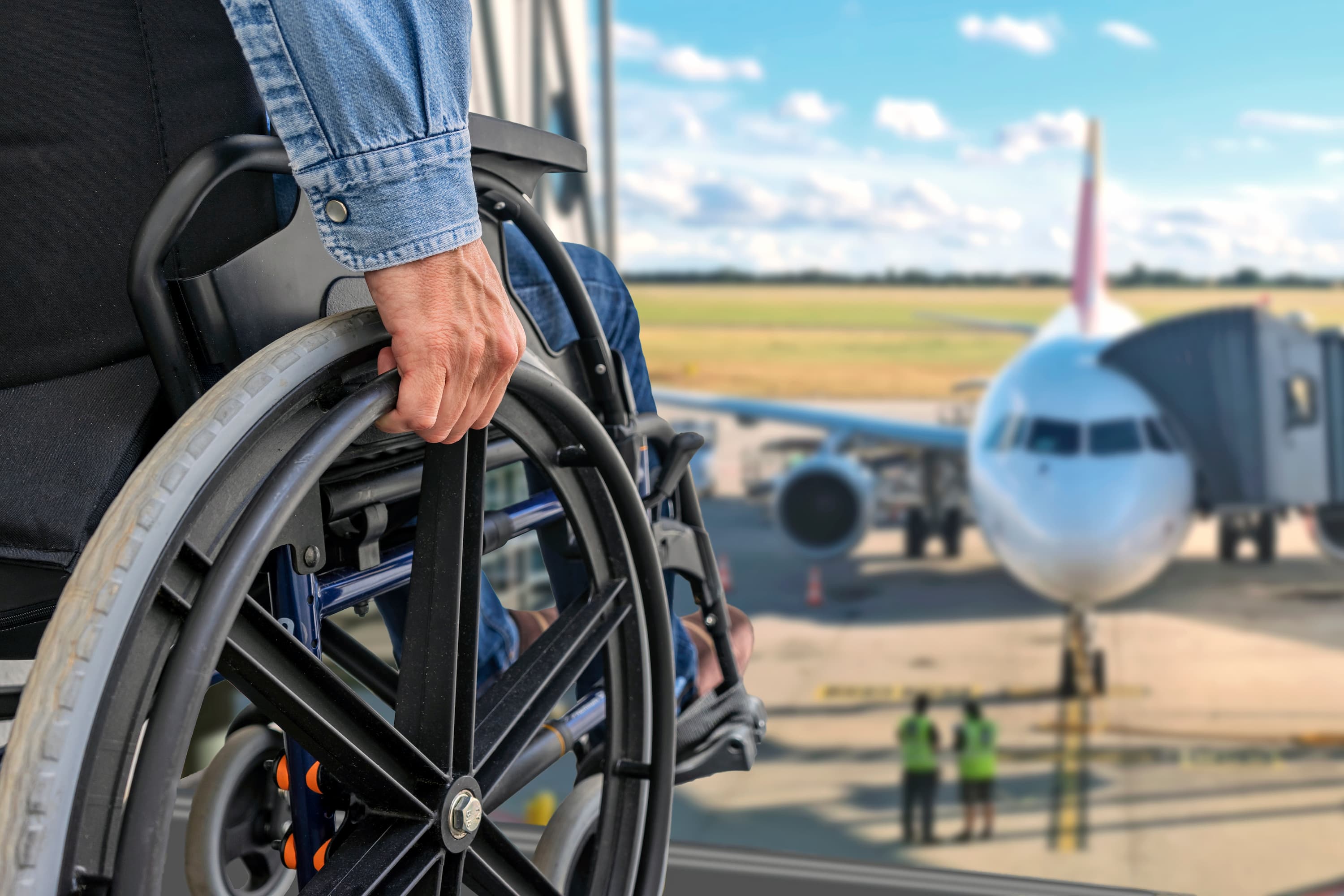 Person in a wheelchair at an airport terminal, with a view of an airplane at the gate in the background.