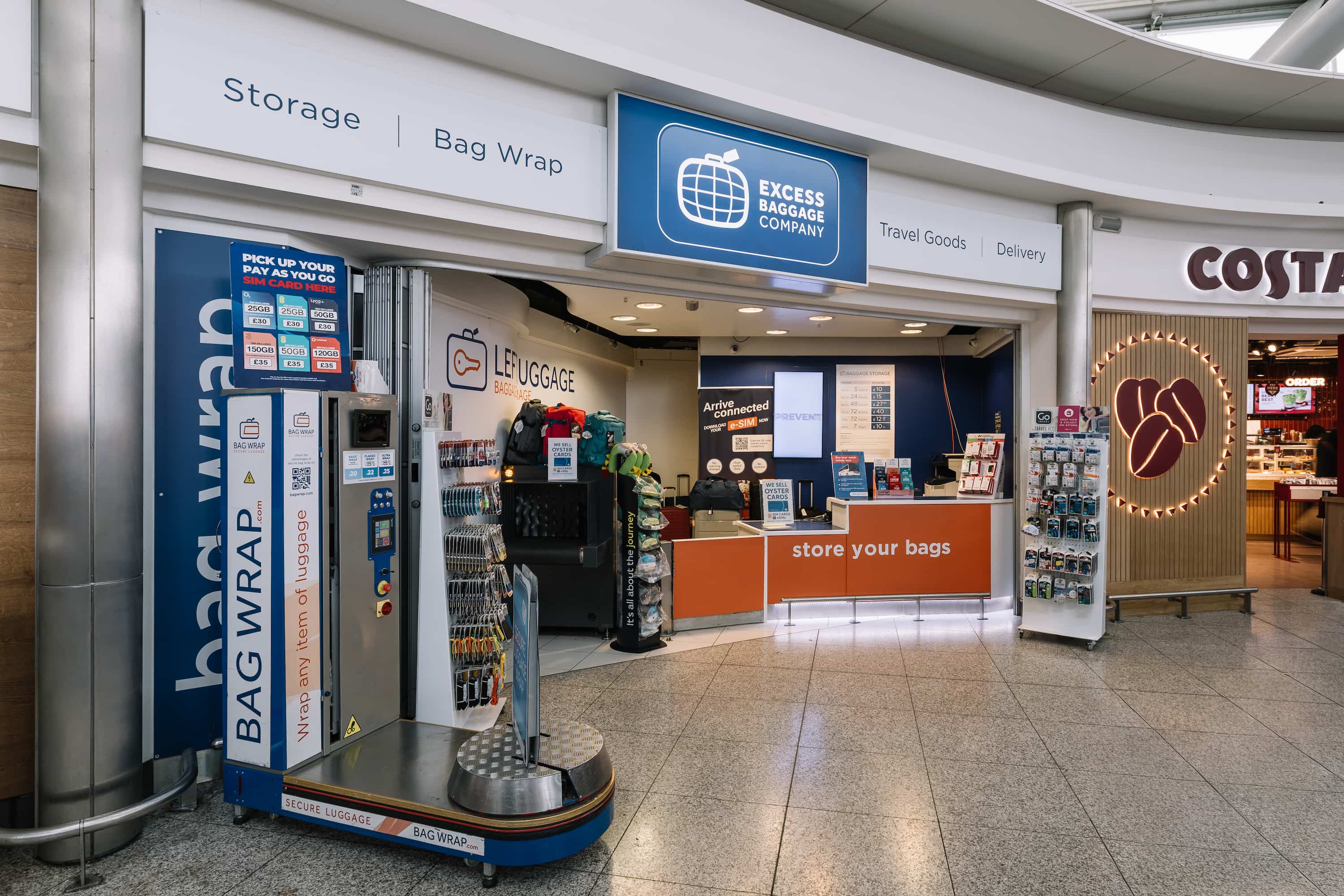 Excess Baggage Company store in an airport offers bag storage, wrapping services, and travel goods. Nearby is a coffee shop with a bright logo.