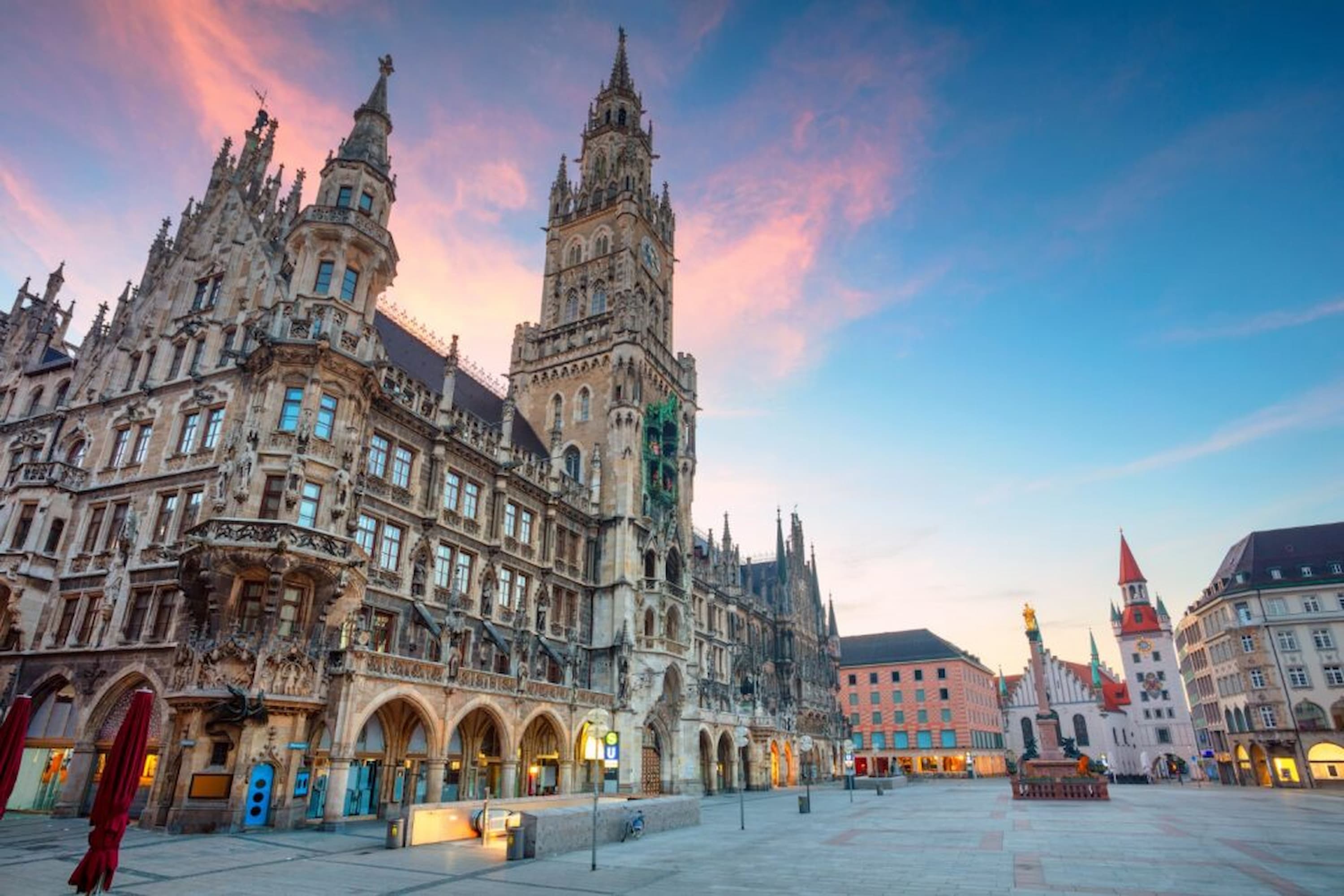 Munich's Marienplatz at sunset, featuring the ornate New Town Hall with its tall clock tower, surrounded by historic buildings.