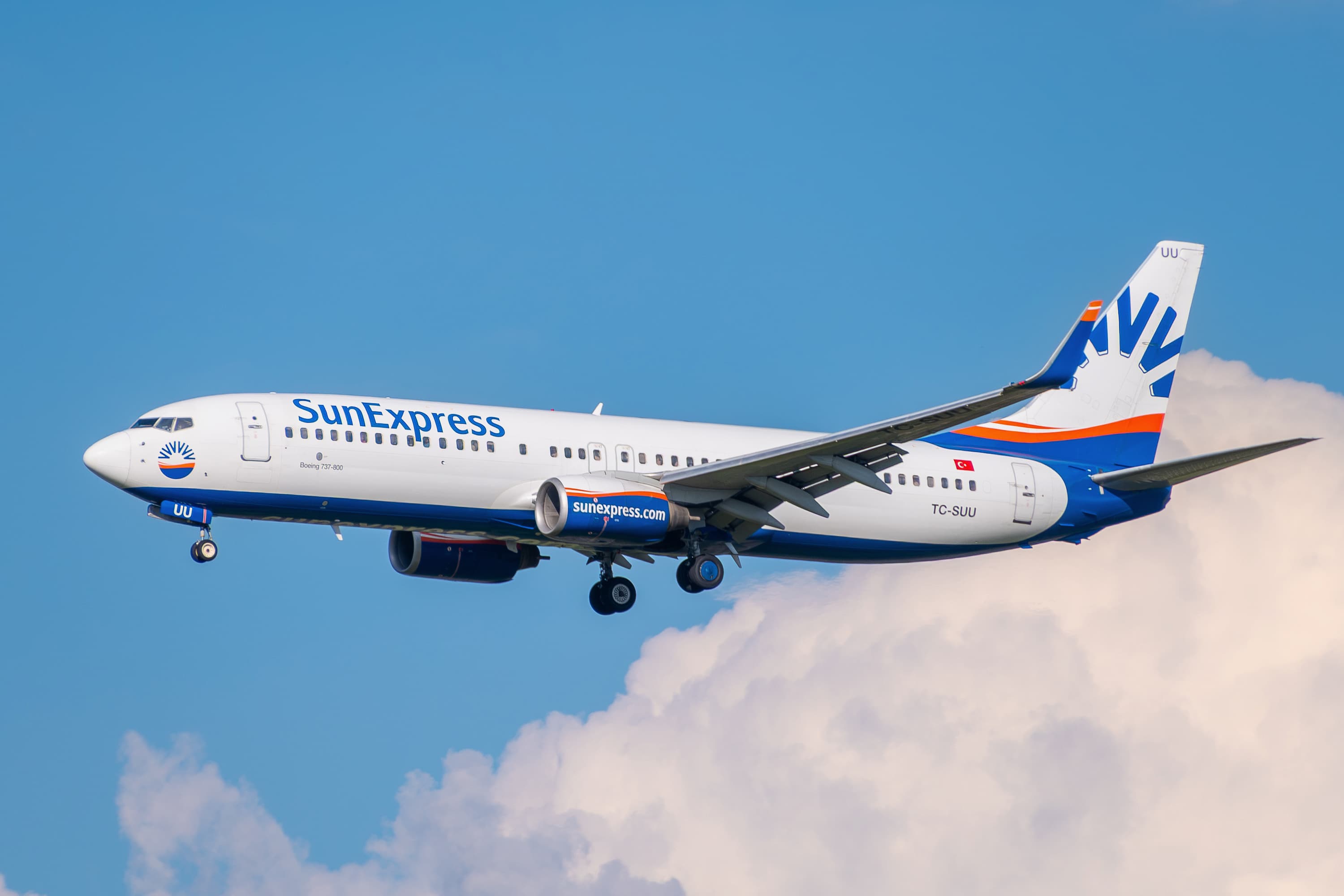 A SunExpress Boeing 737-800 airplane flying against a clear blue sky with some clouds.