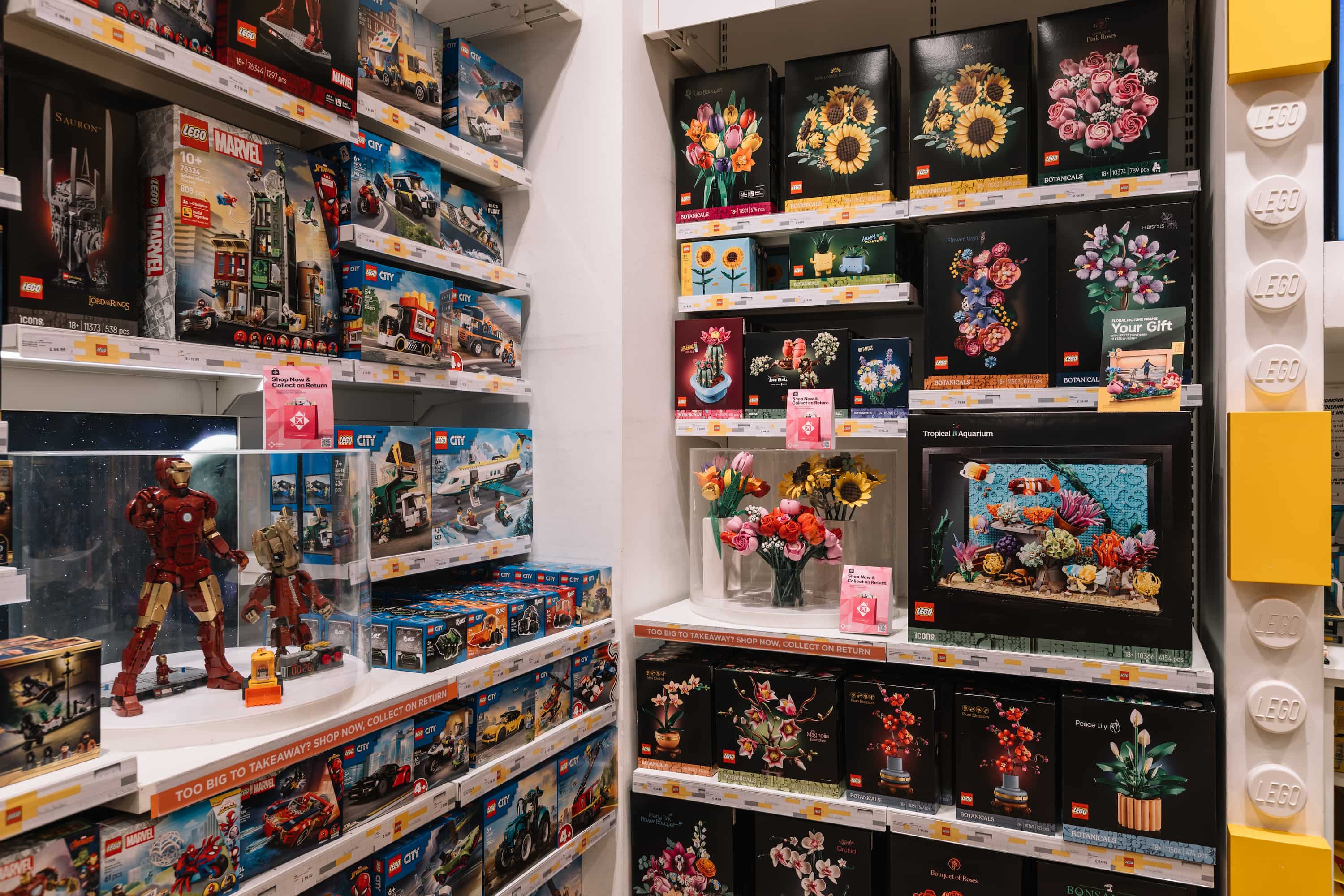 A store shelf filled with various LEGO sets, including Marvel figures and botanical designs, with colourful displays of LEGO flowers.