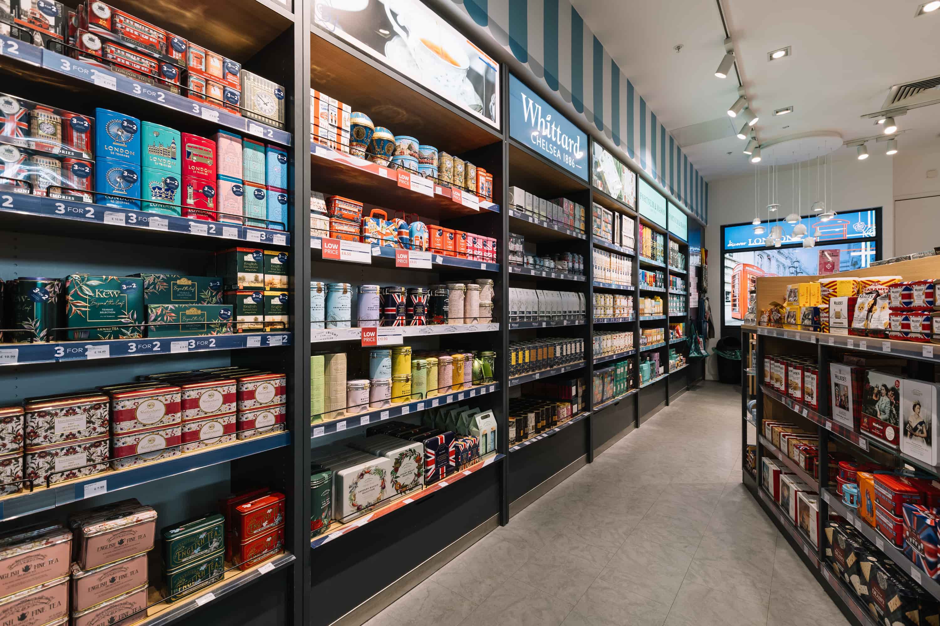 A store aisle filled with assorted tea tins and boxes on shelves. Signs display offers like "3 for 2" and "Low Price" under bright lighting.