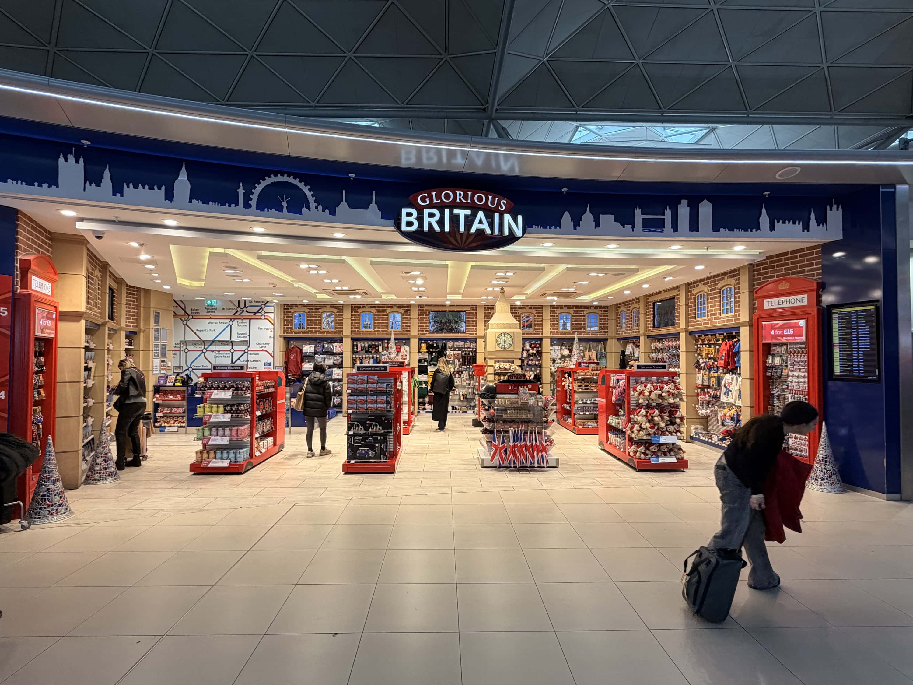 A gift shop named "Glorious Britain" with British-themed souvenirs, red displays, and a mock phone booth inside a large, well-lit shopping area.