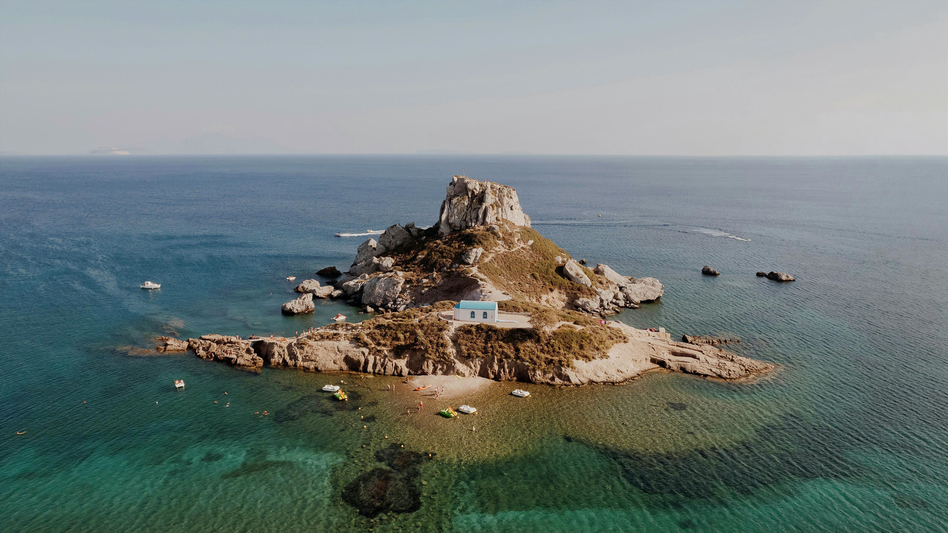  Rocky island with a quaint house with sandy path leading to boats on the shore and linking to guide to Kos