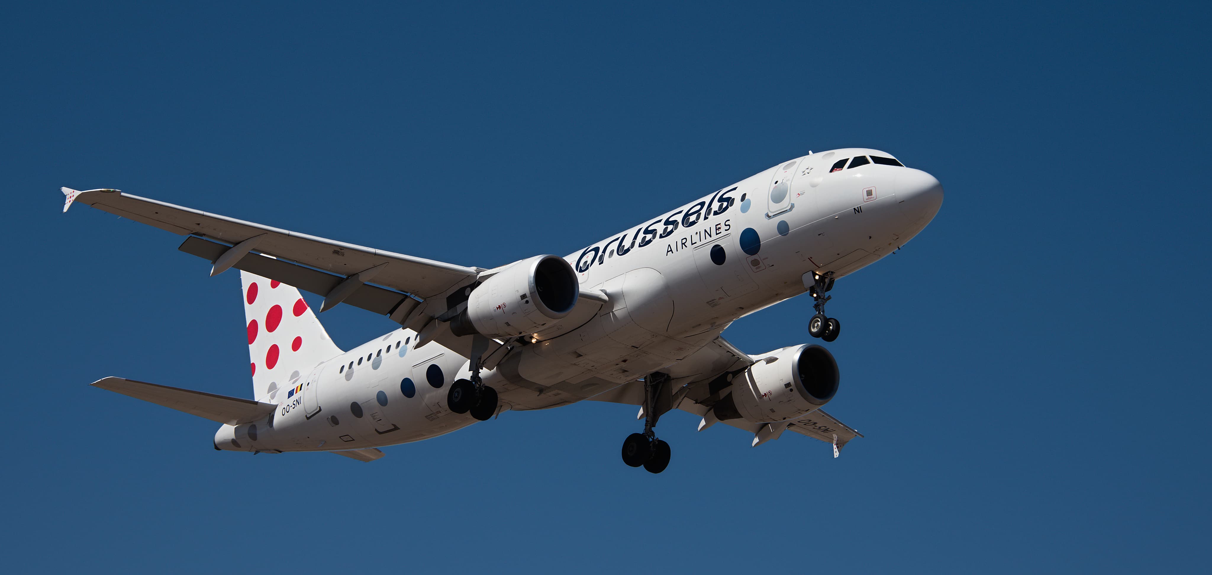 A Brussels Airlines jet with red polka dots on the tail flying against a clear blue sky.