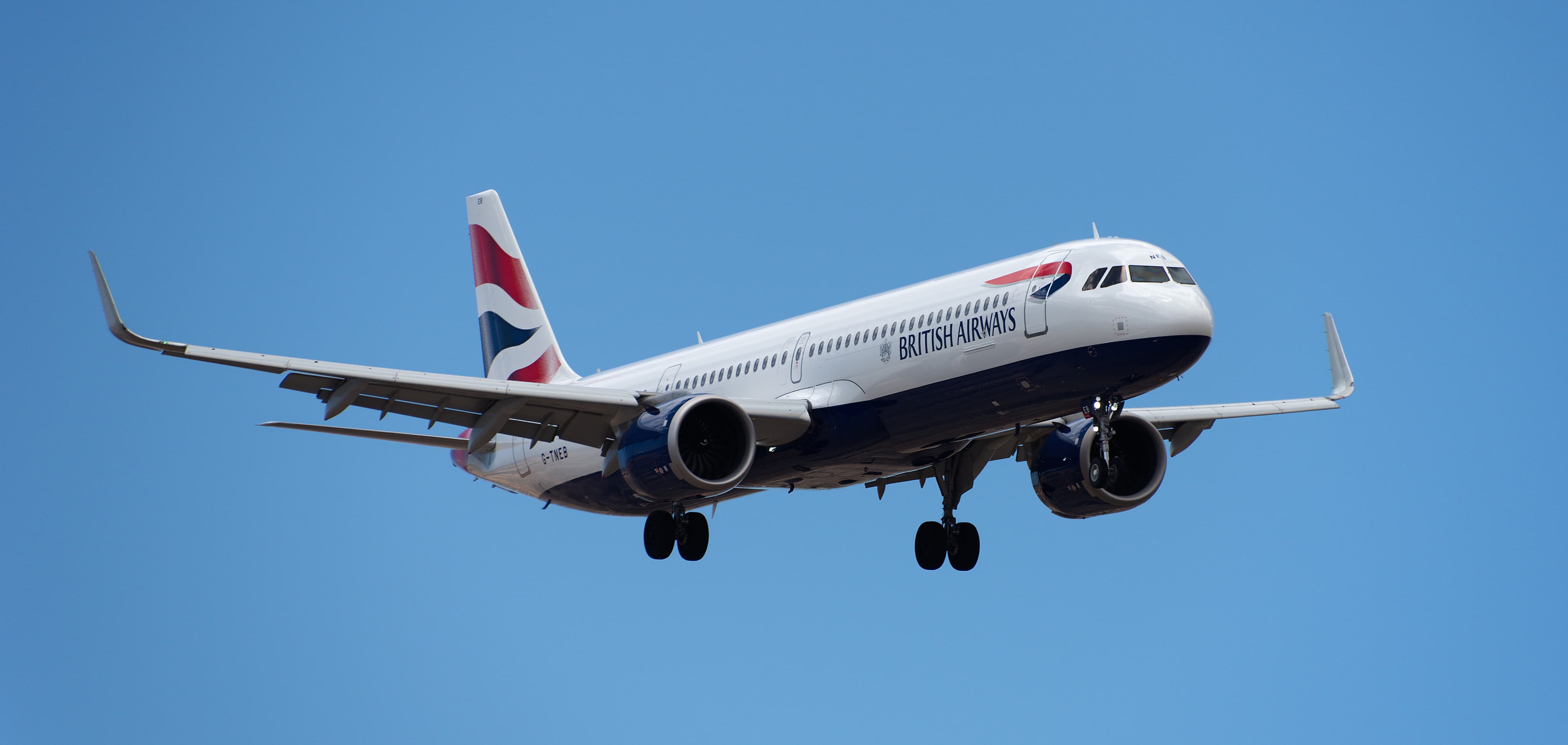 A British Airways airplane in flight with landing gear deployed against a clear blue sky.