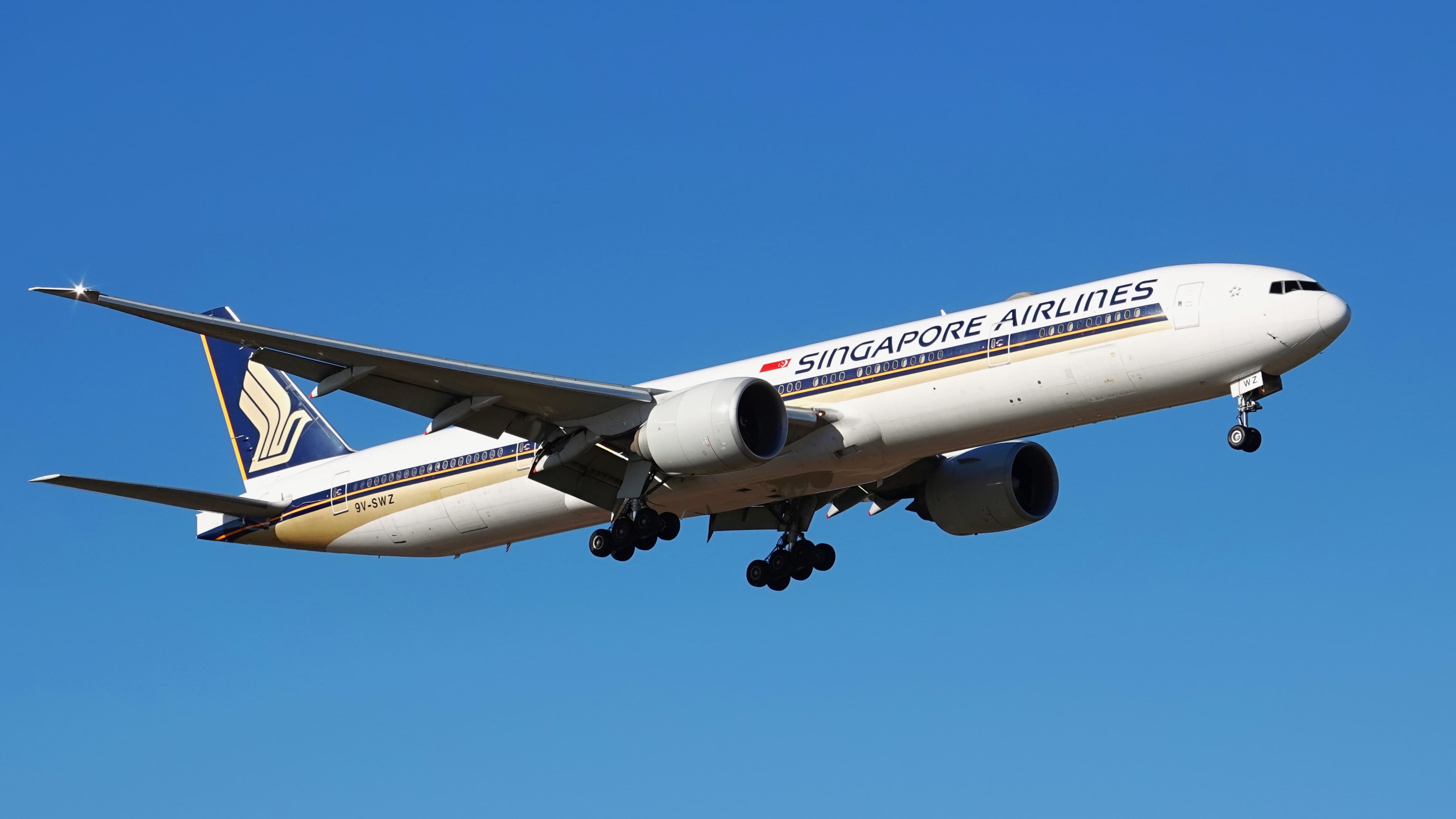 A Singapore Airlines airplane flying against a clear blue sky with landing gear extended.