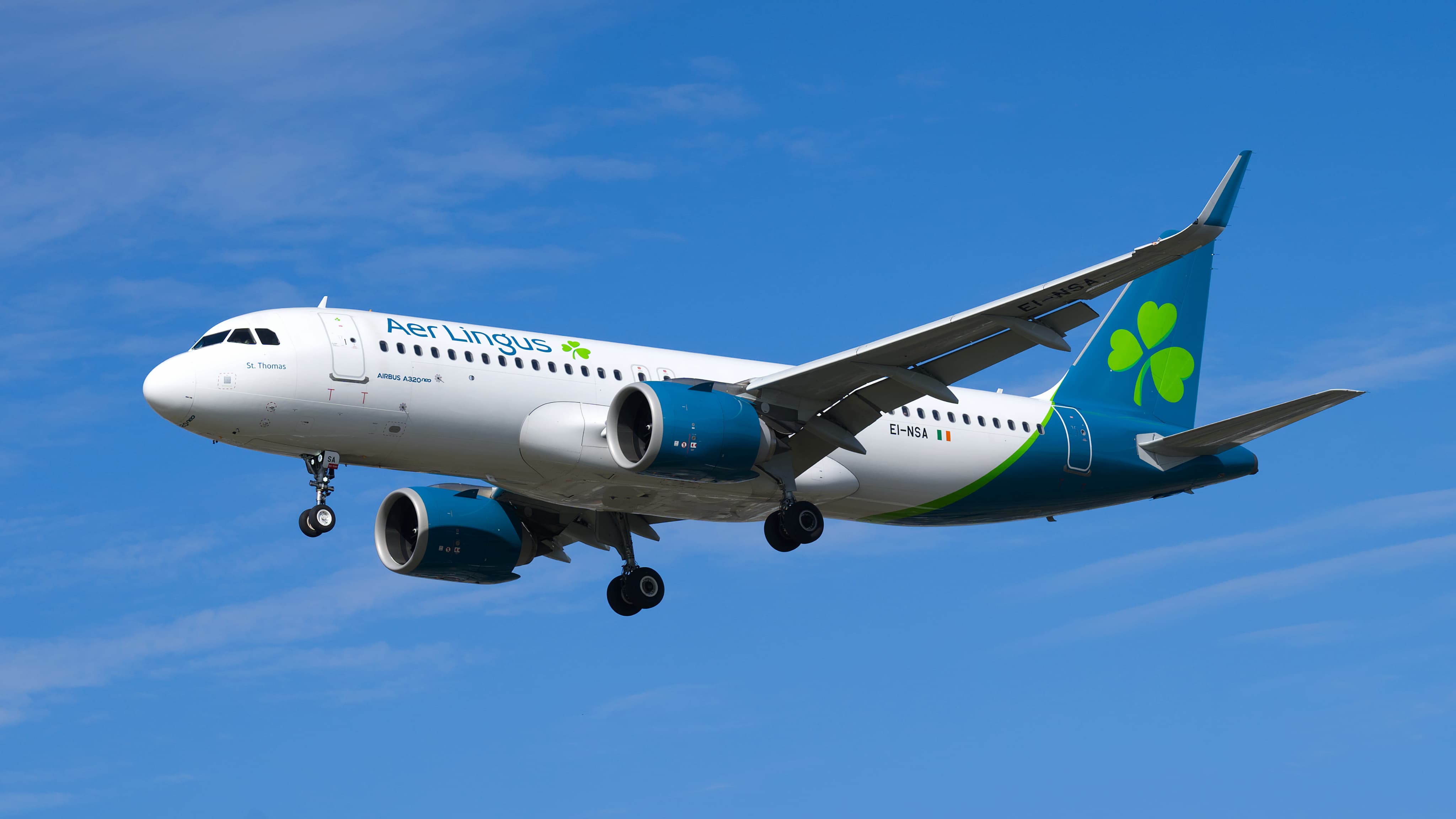 Aer Lingus Airbus A320neo in flight with landing gear extended against a clear blue sky.