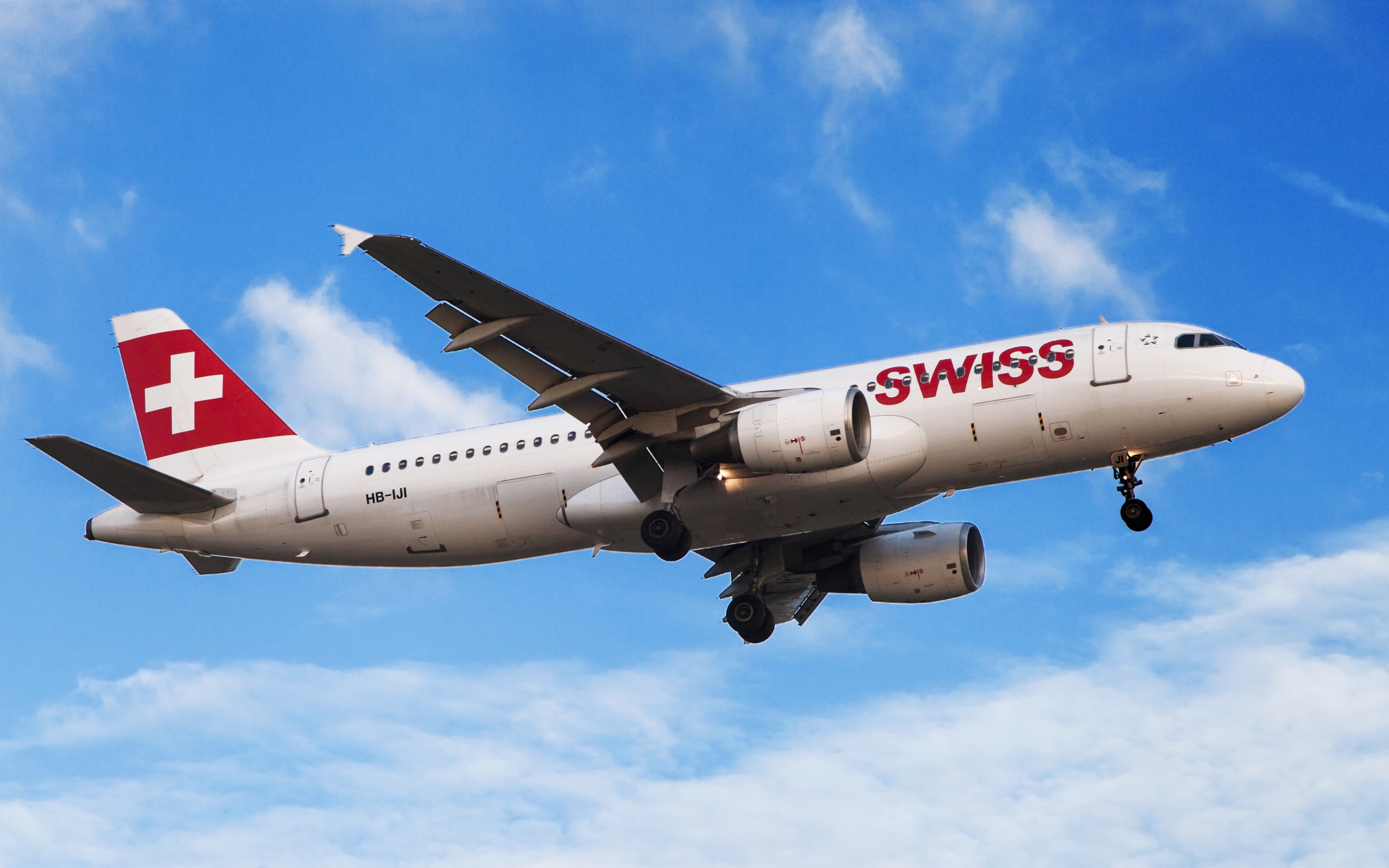 Swiss Airlines airplane in flight against a blue sky, showing landing gear lowered and red tail with white cross.