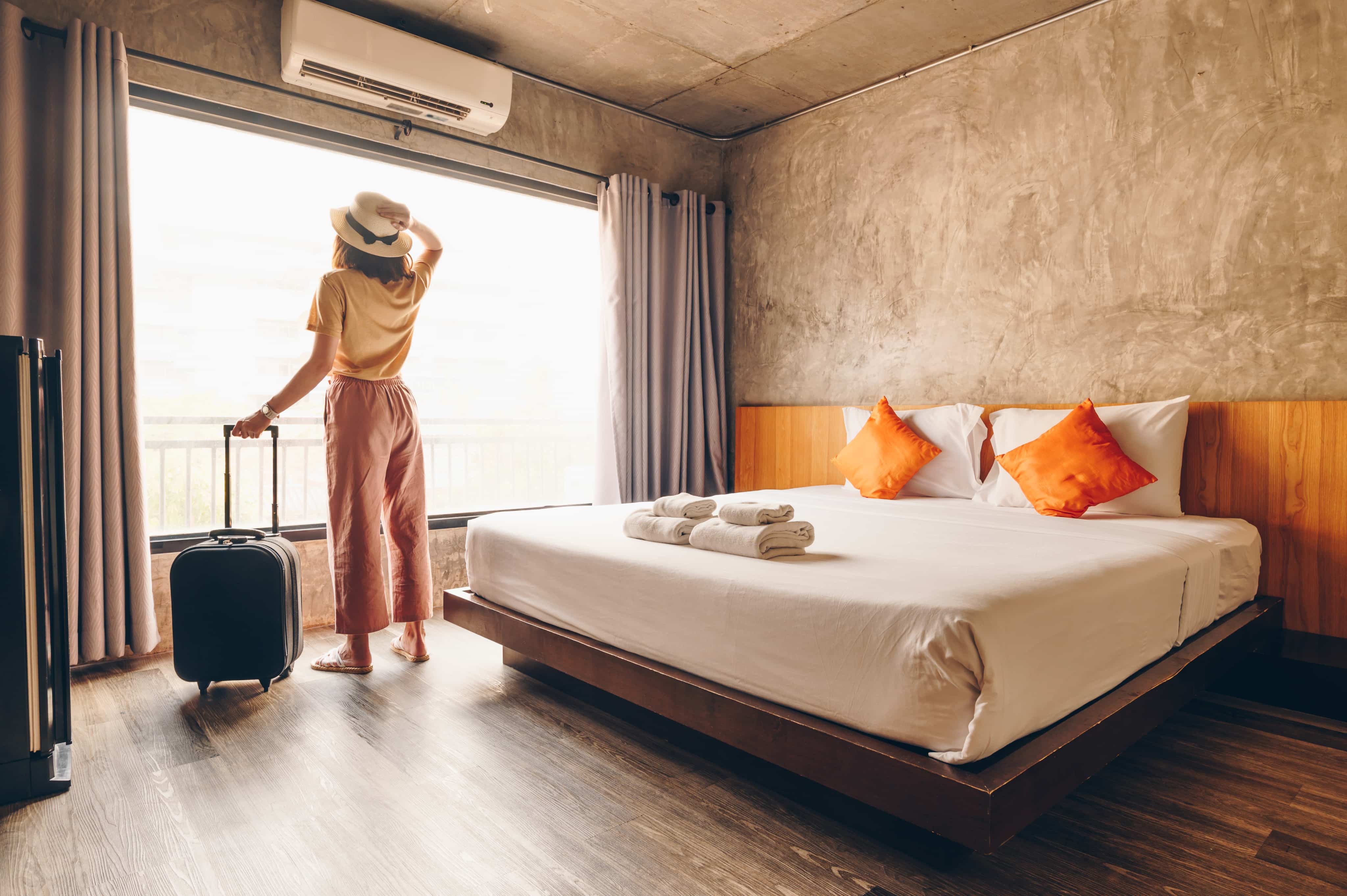 Woman holding suitcase and looking out of hotel room window