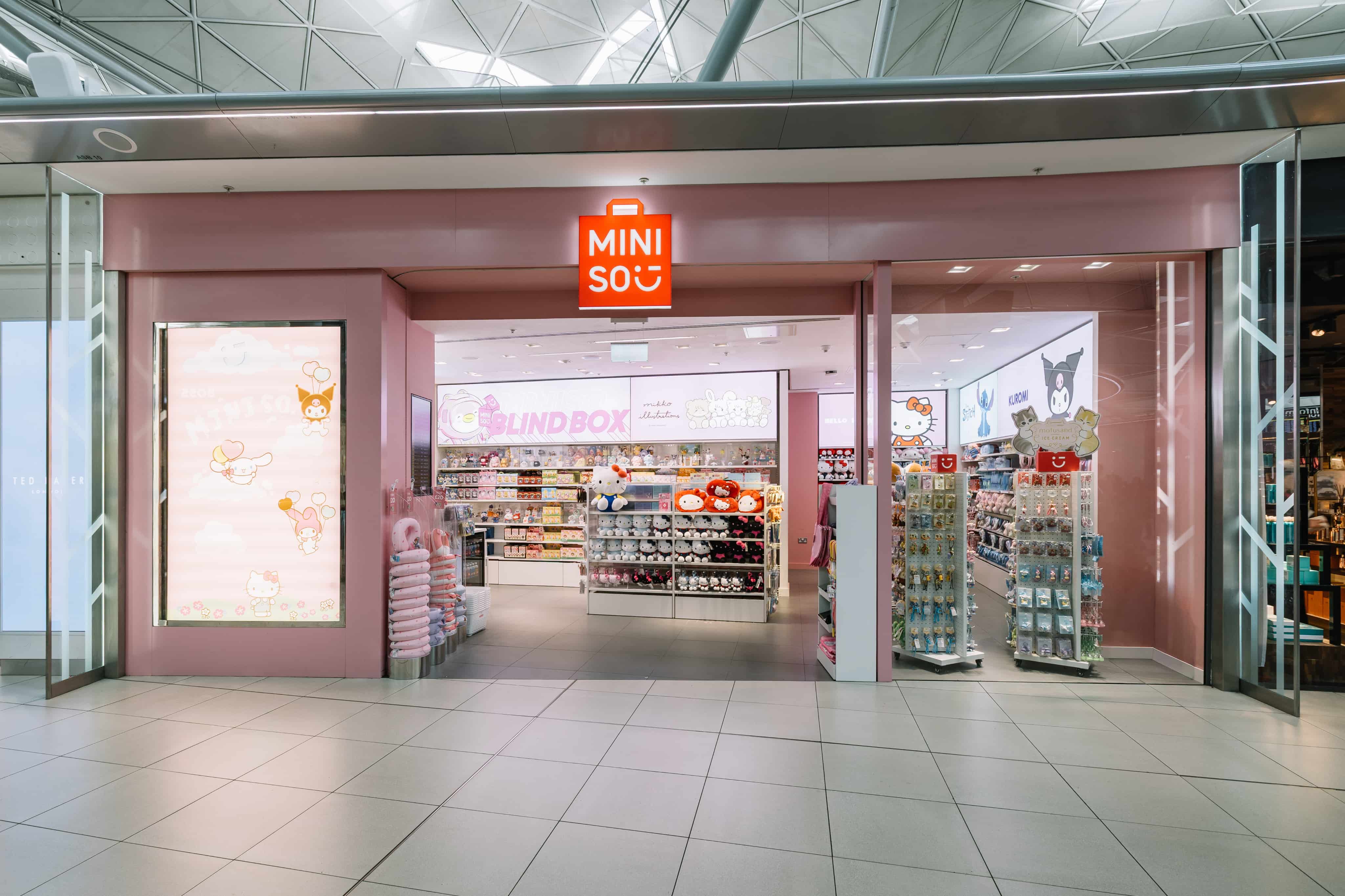 Exterior view of a Miniso store with pink décor, featuring shelves stocked with plush toys and various products inside.