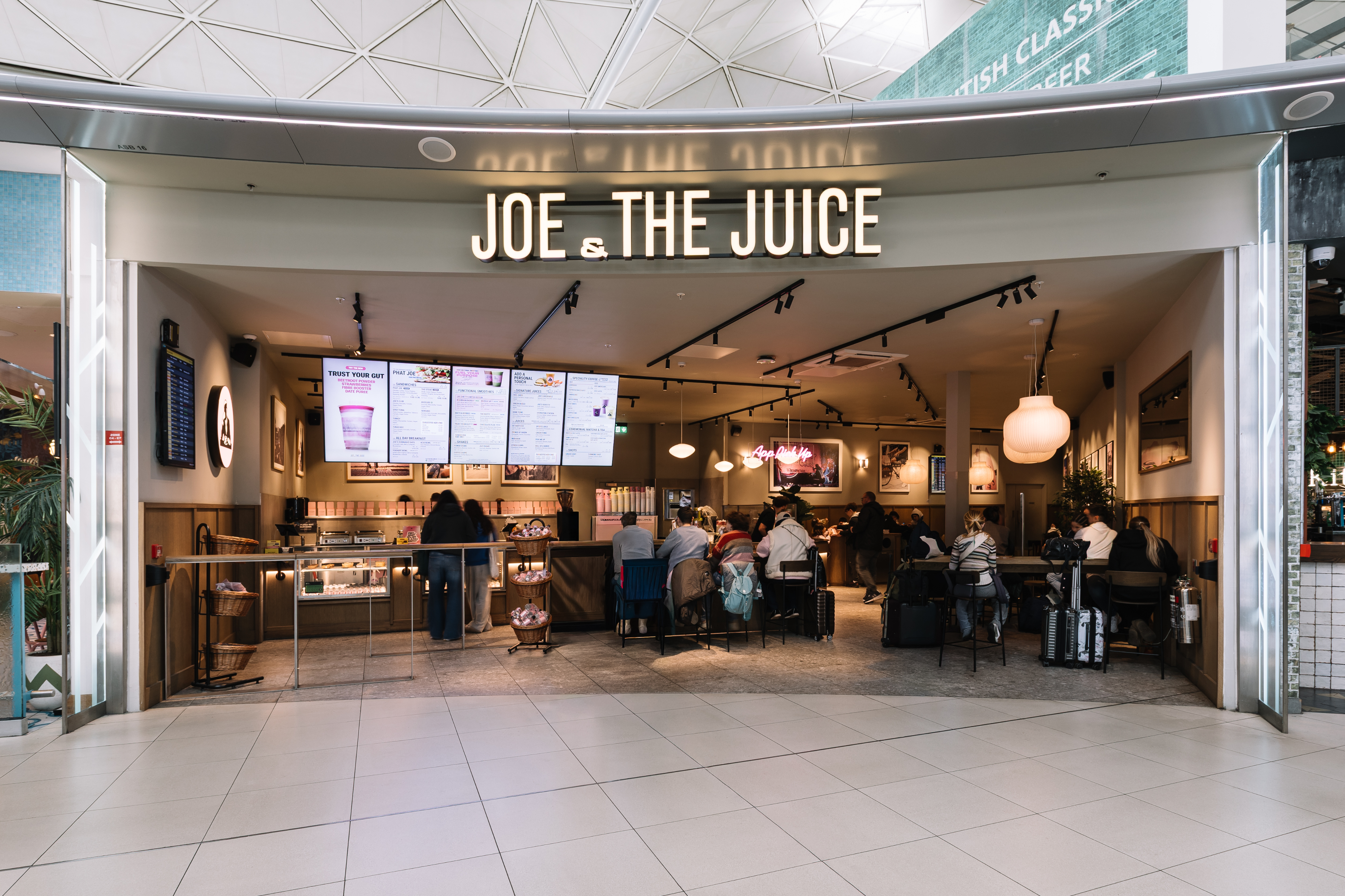 People sitting inside a Joe & The Juice café with a large menu display and soft lighting, creating a cosy atmosphere.