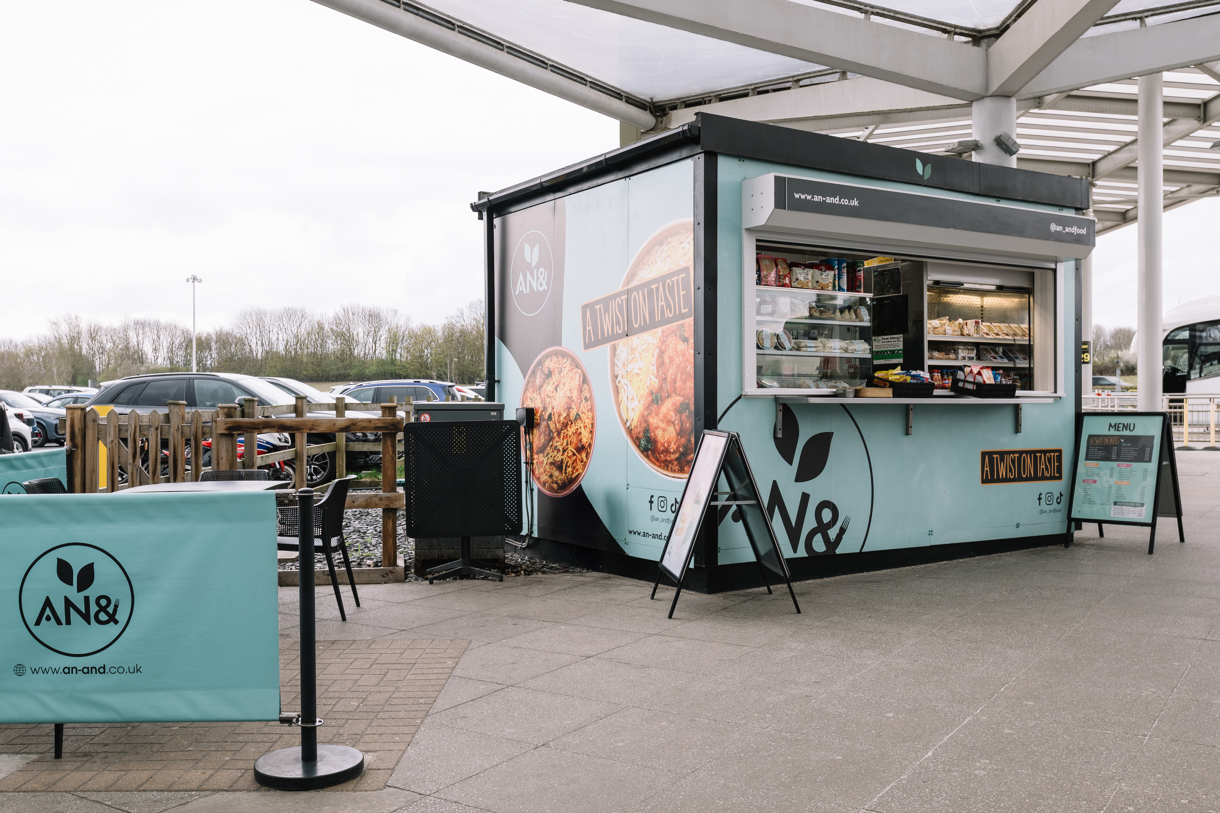 A modern food kiosk with "A Twist on Taste" slogan, displaying snacks and beverages. Outdoor seating is available nearby.