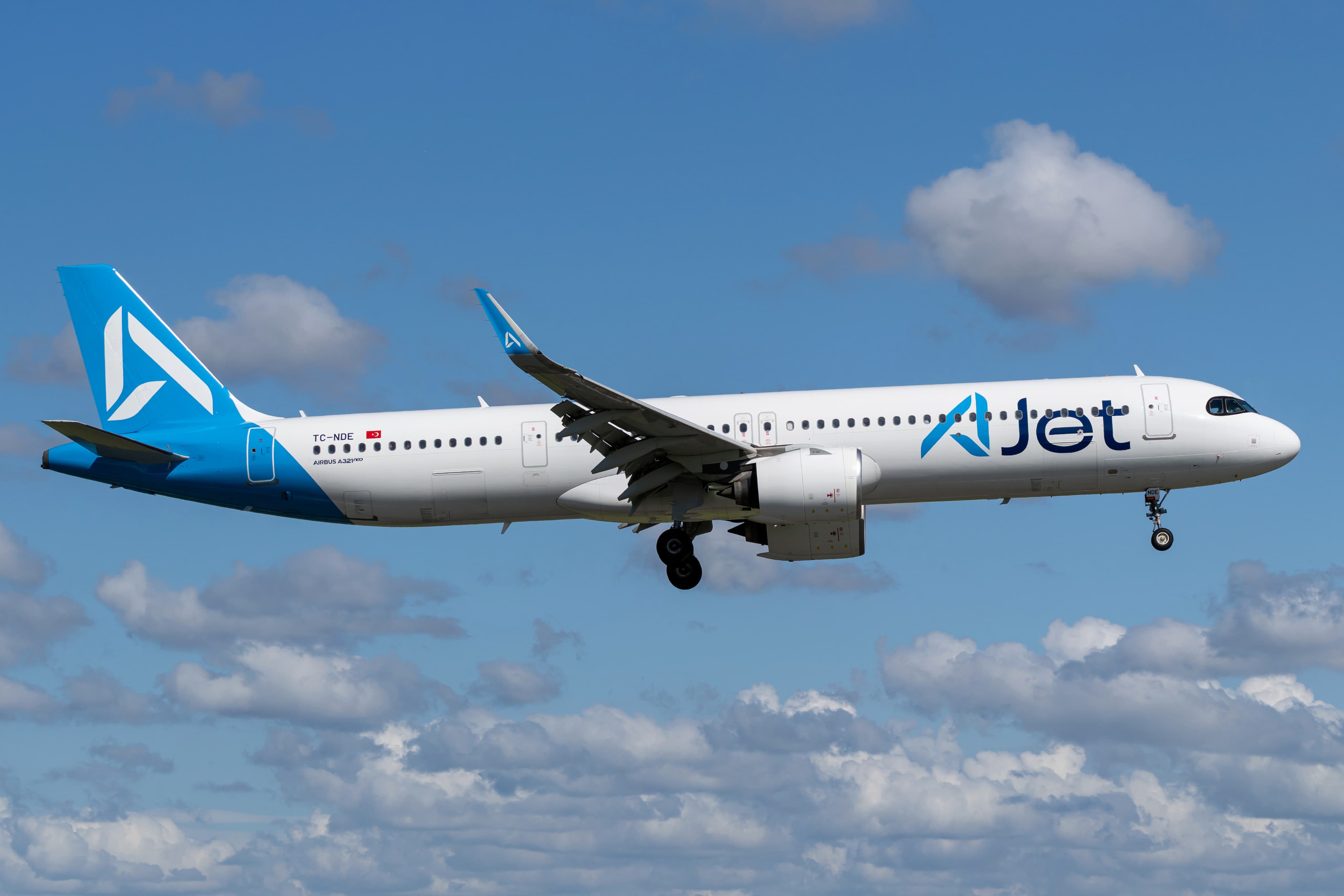 An Airbus A321neo airplane with "Jet" branding, featuring blue and white livery, flying against a partly cloudy sky.