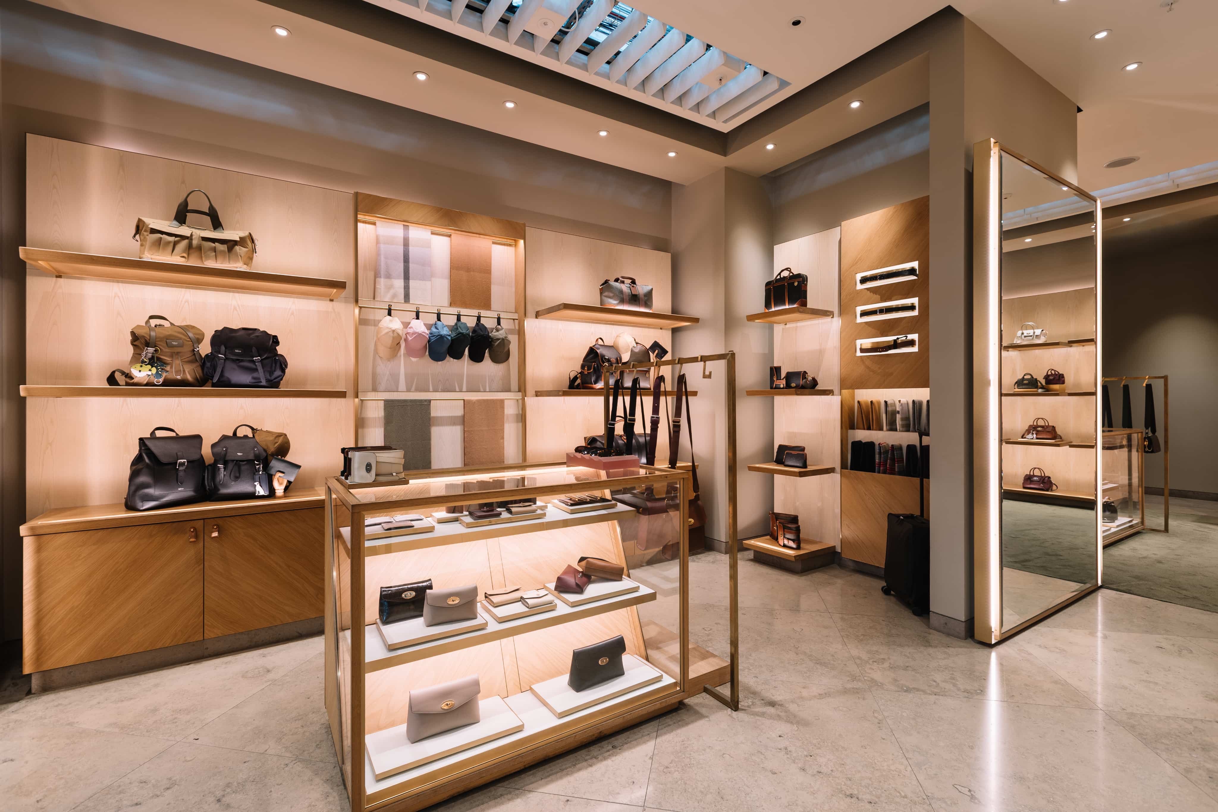 Luxury boutique interior featuring handbags, wallets, and accessories displayed on wooden shelves and a glass case, with soft lighting.