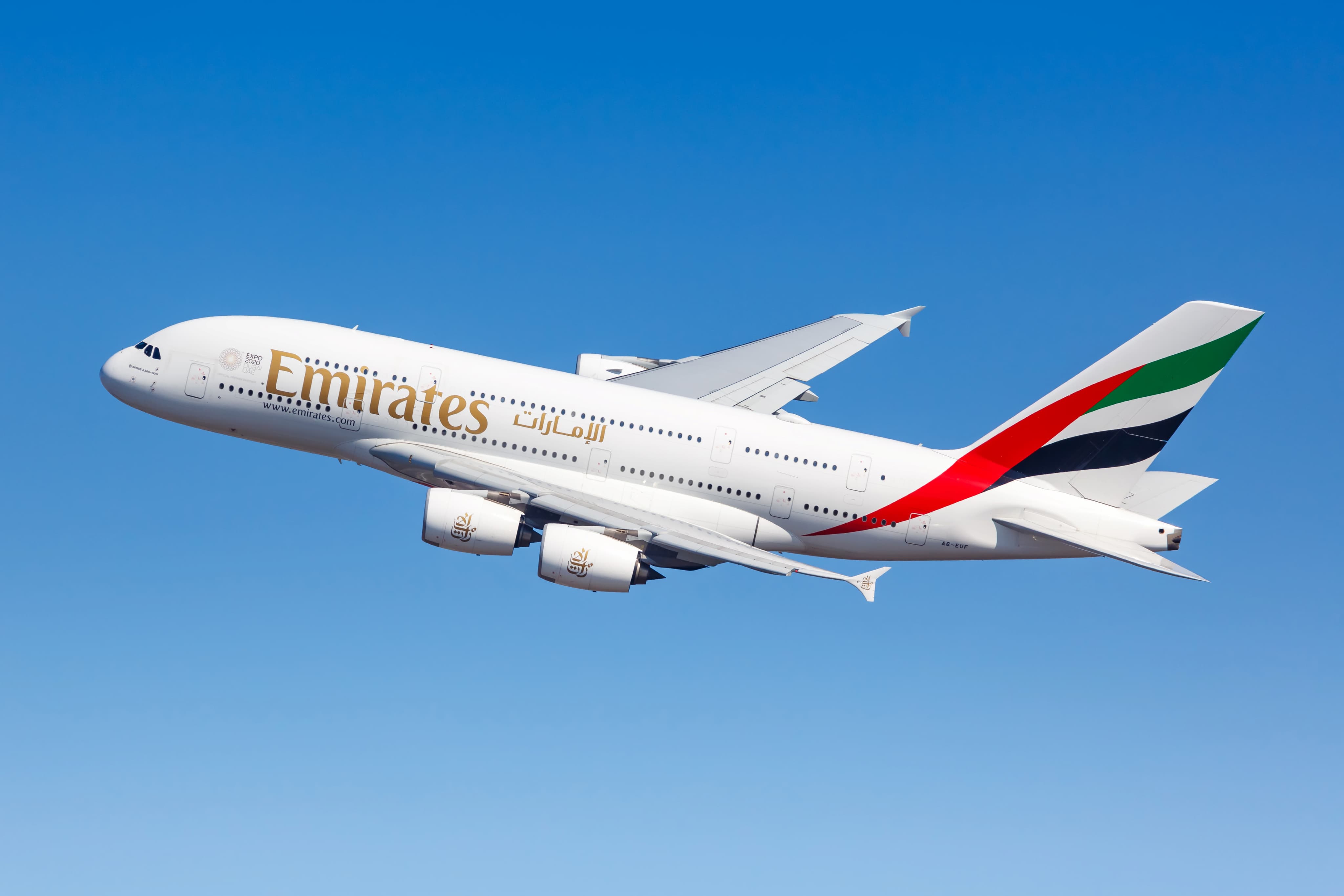 An Emirates Airbus A380 aircraft flying against a clear blue sky.