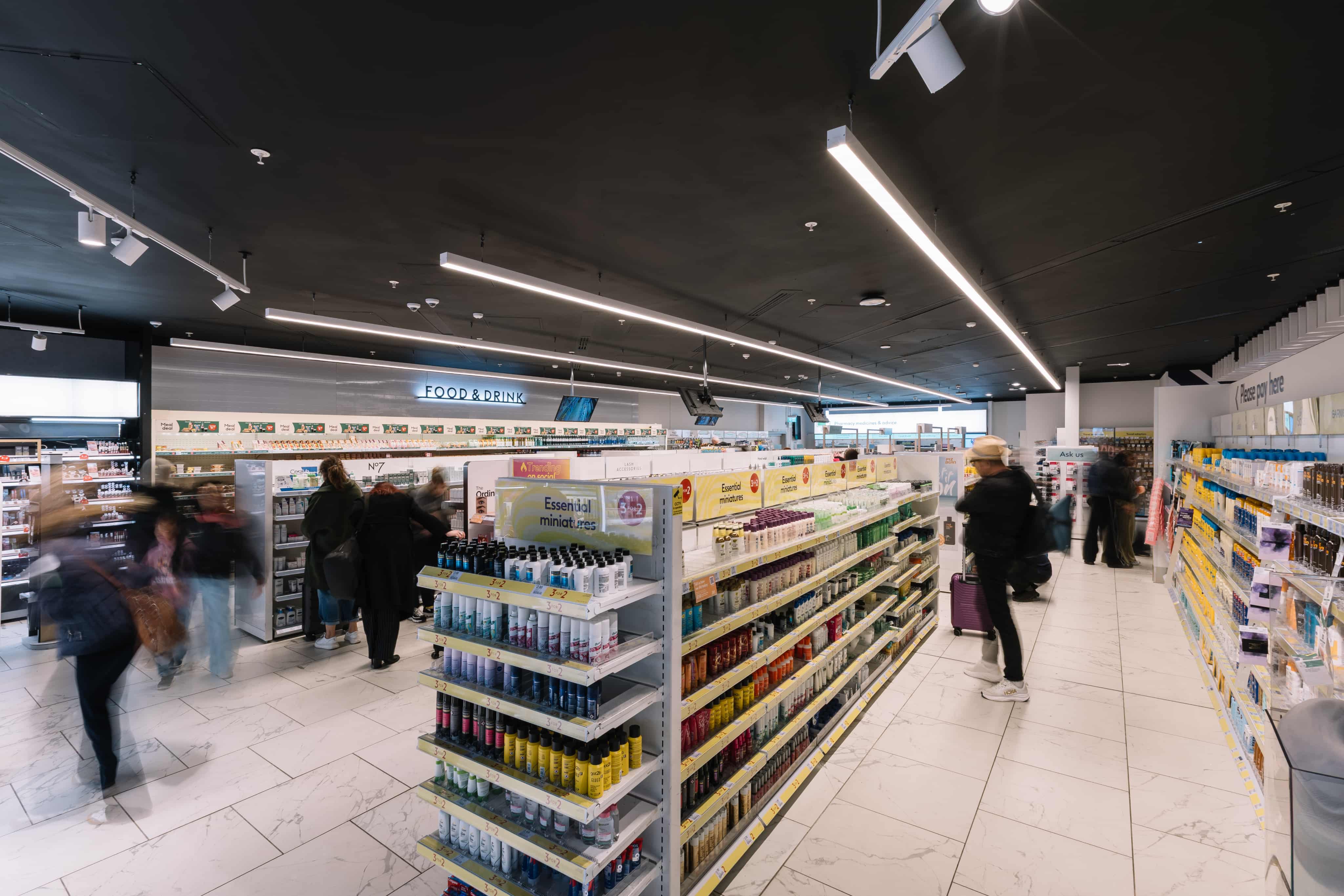People browse aisles in a brightly lit shop with shelves stocked with health and beauty products.
