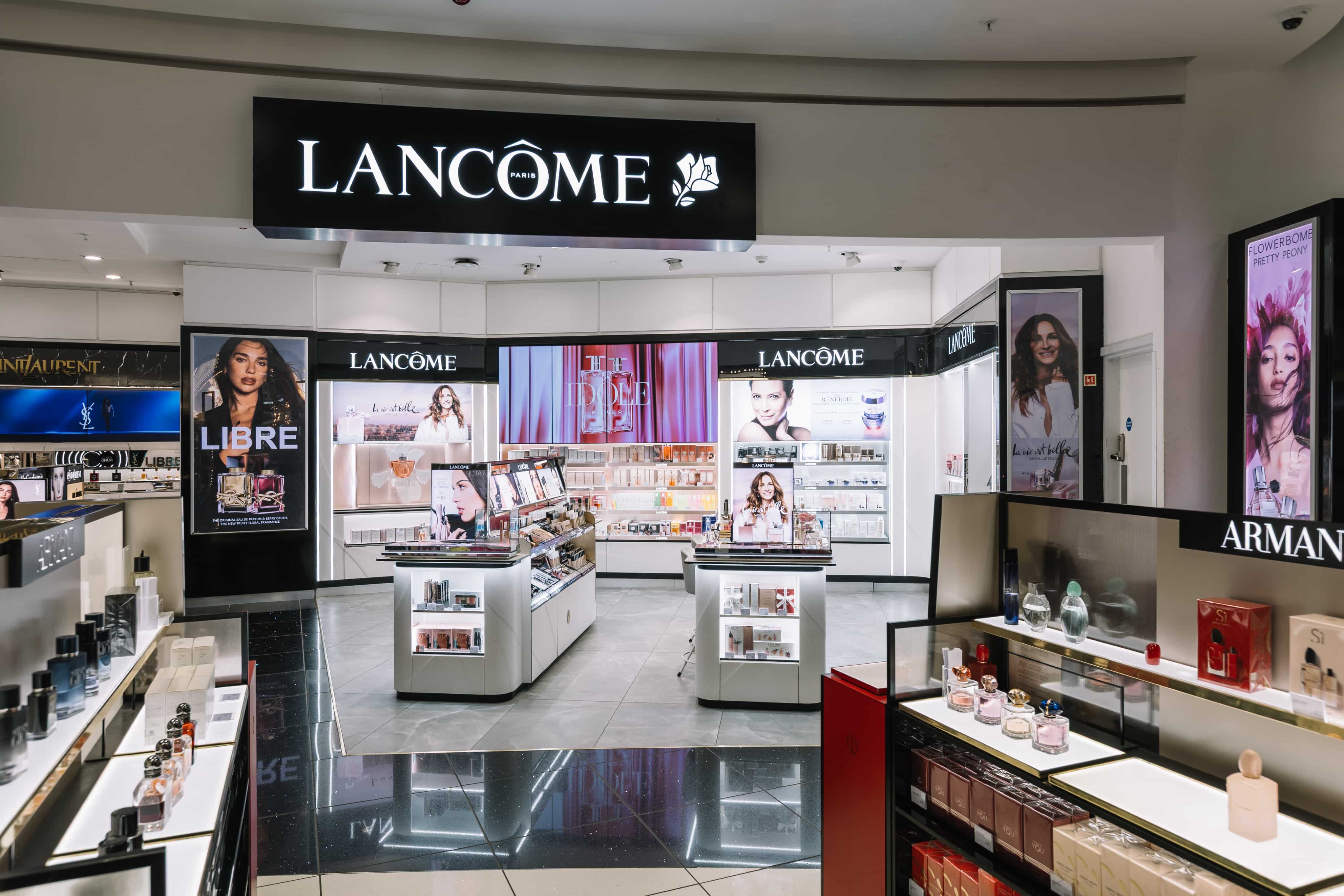 Lancome store interior featuring cosmetics and perfumes, with illuminated displays and promotional posters on white and black fixtures.