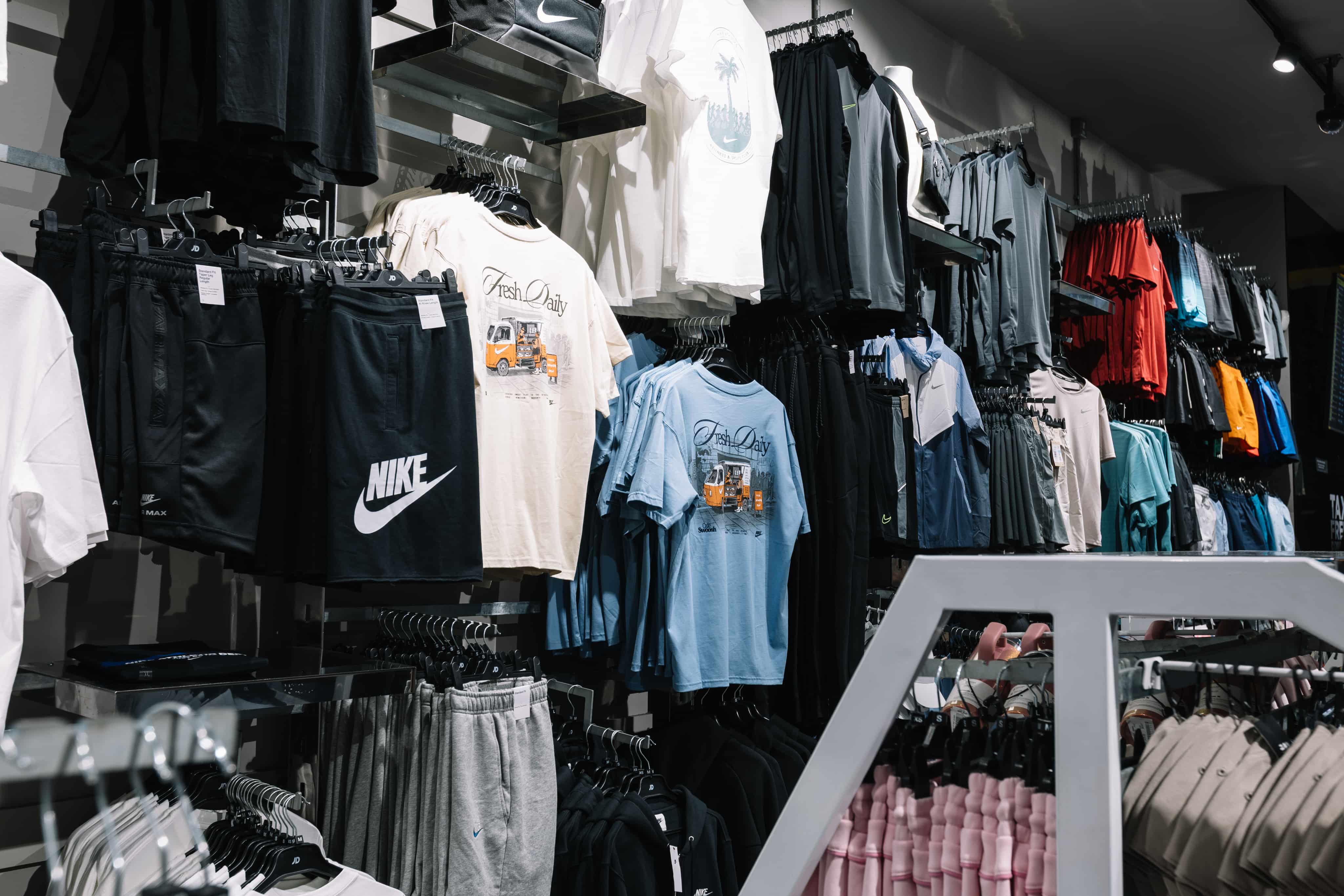 Clothing store display featuring sportswear, including Nike shorts, graphic tees, and various activewear in monochrome and vibrant colours.
