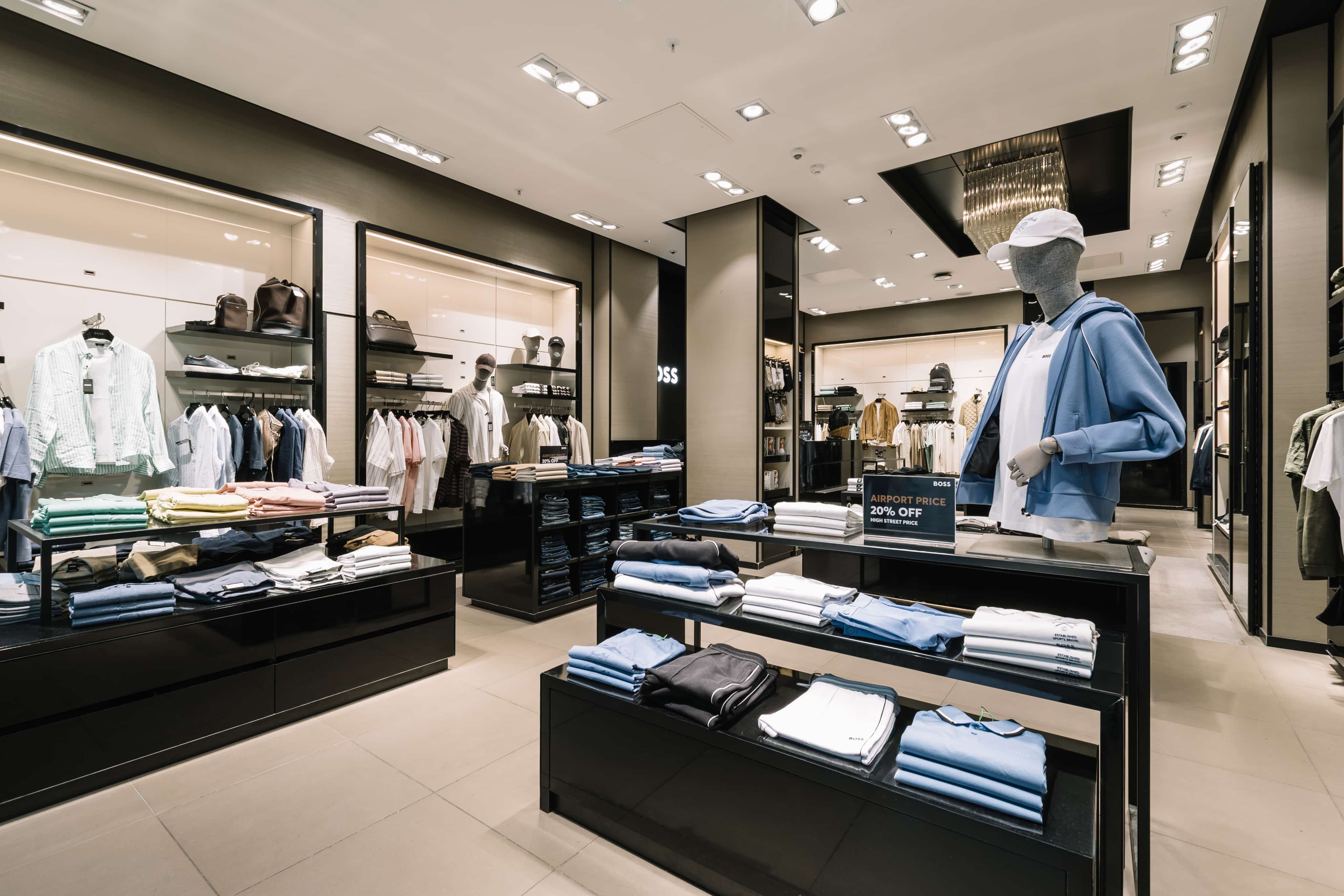 Clothing store interior with neat racks of folded clothes, a mannequin in a blue jacket, and a sign advertising a 20% discount.
