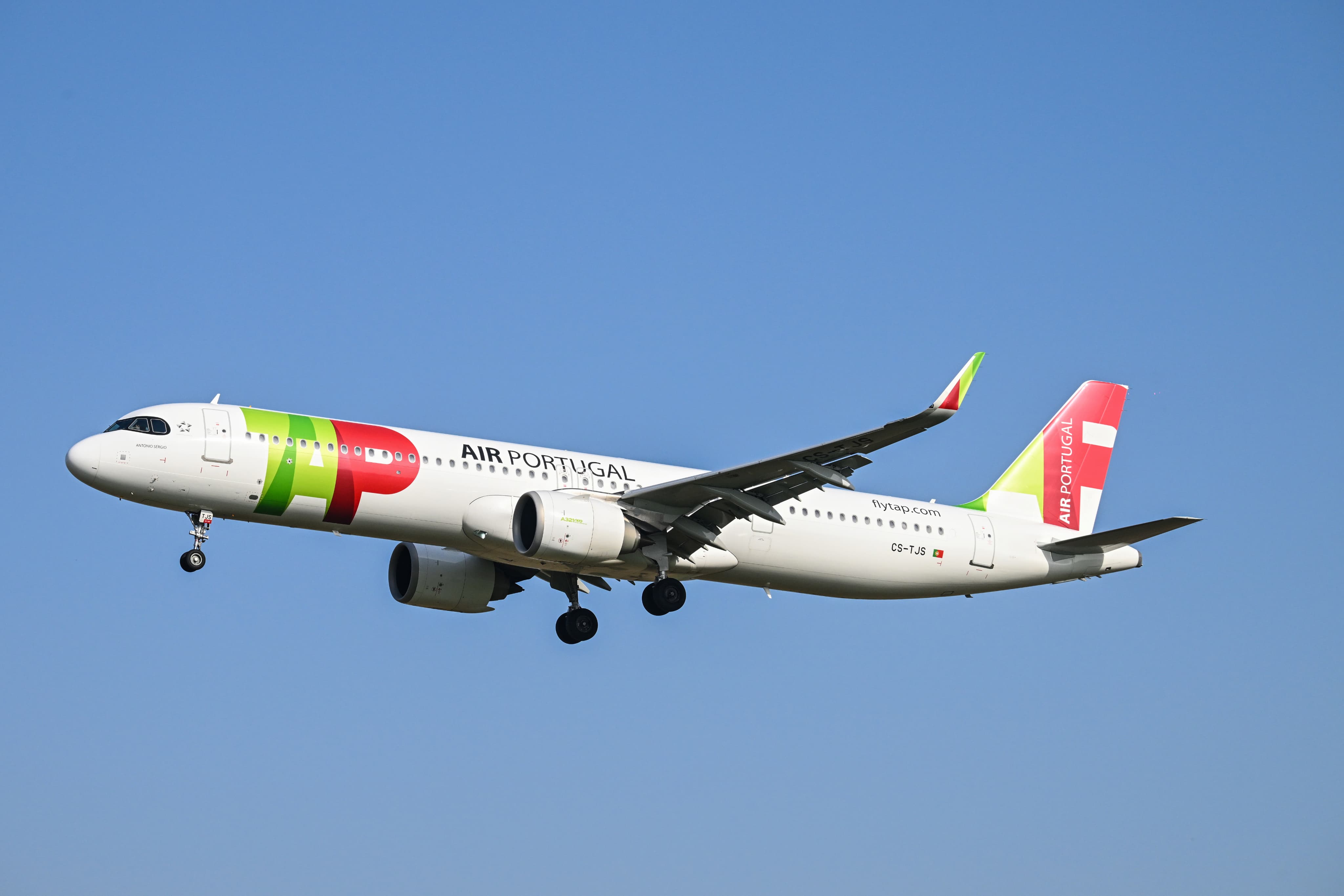 An Air Portugal aircraft featuring a red, green, and white livery, flying against a clear blue sky.
