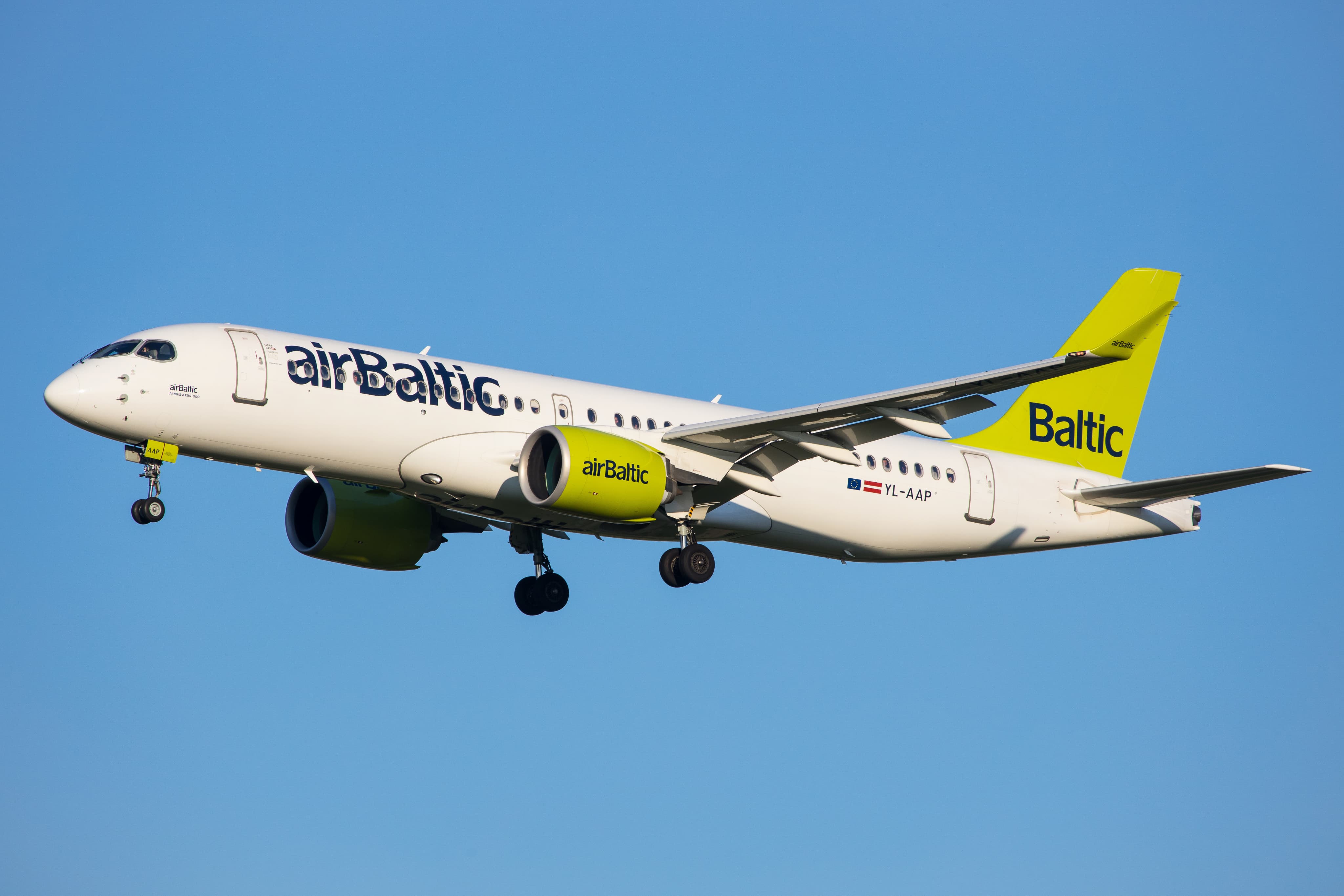 AirBaltic airplane with green engines and tail, flying against a clear blue sky.