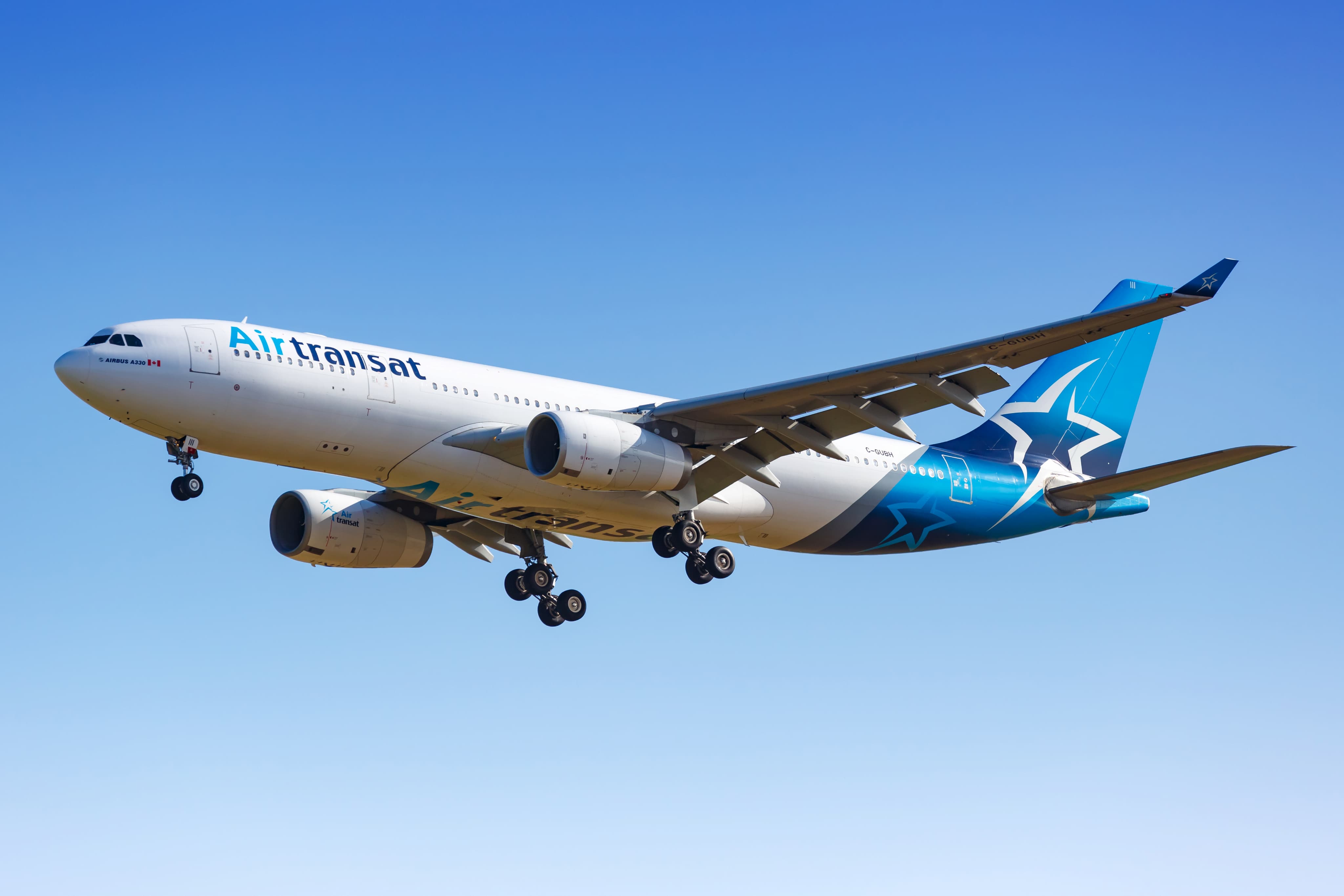 An Air Transat Airbus A330 with landing gear down is flying against a clear blue sky.
