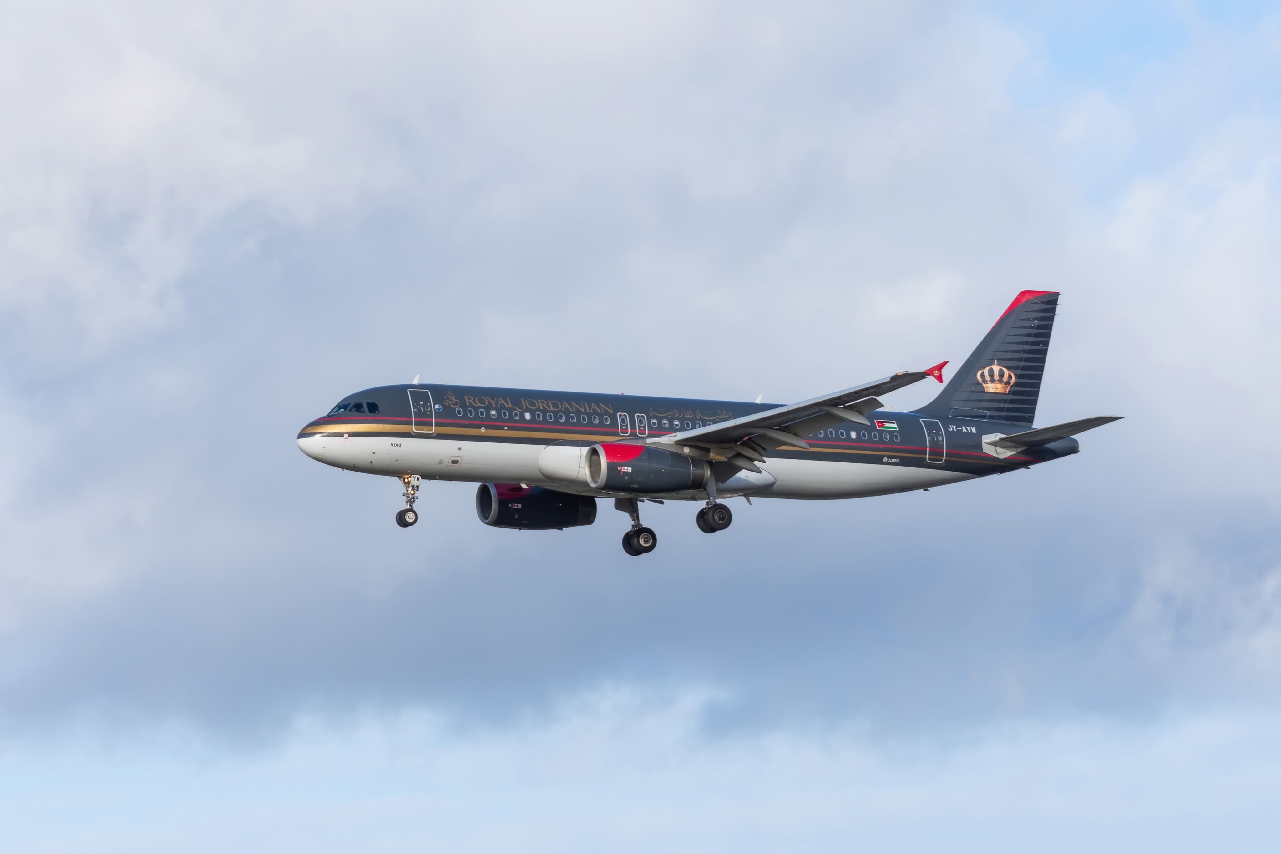 Passenger airplane in Royal Jordanian livery flying against a cloudy sky.