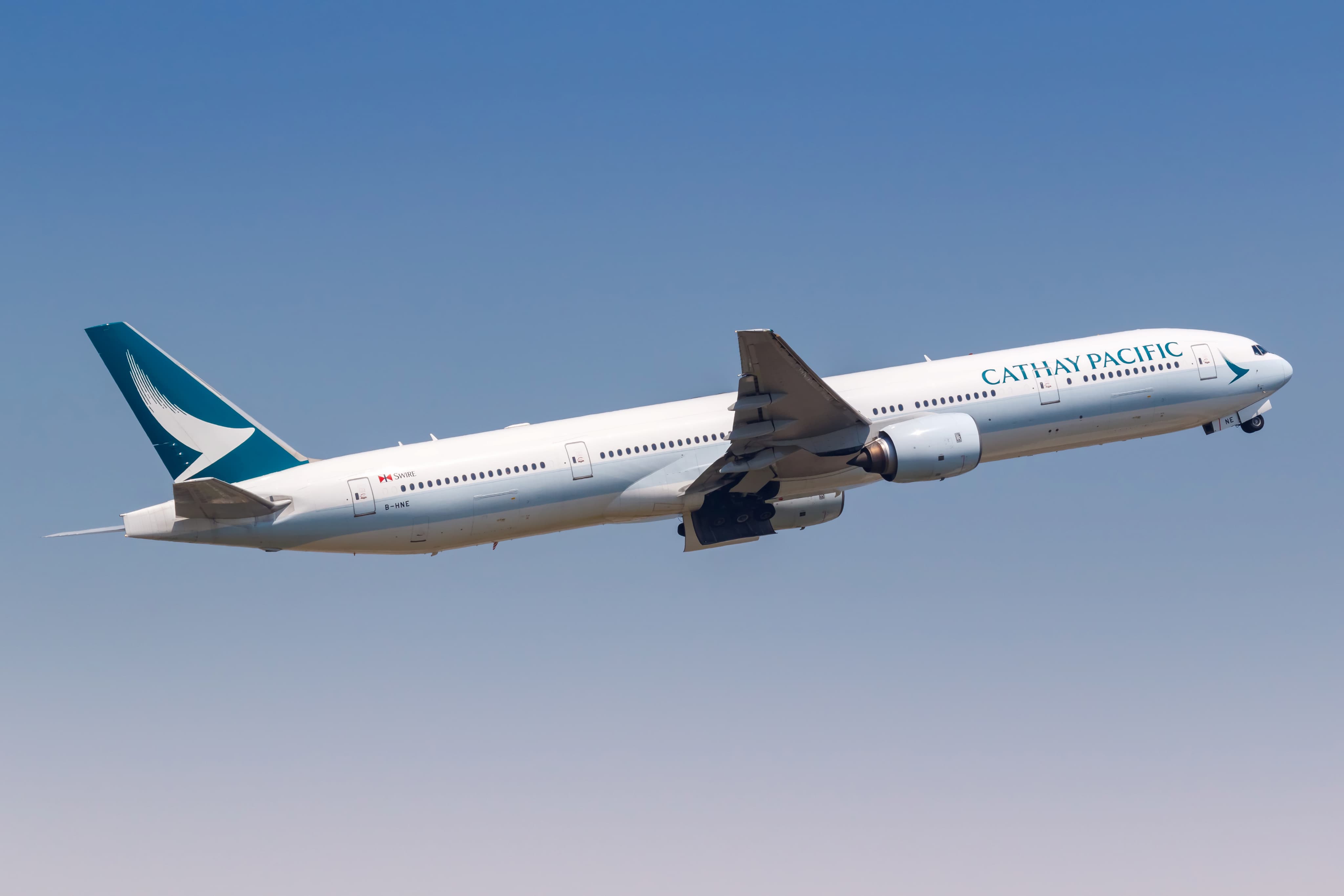 A Cathay Pacific airplane in flight, ascending against a clear blue sky.