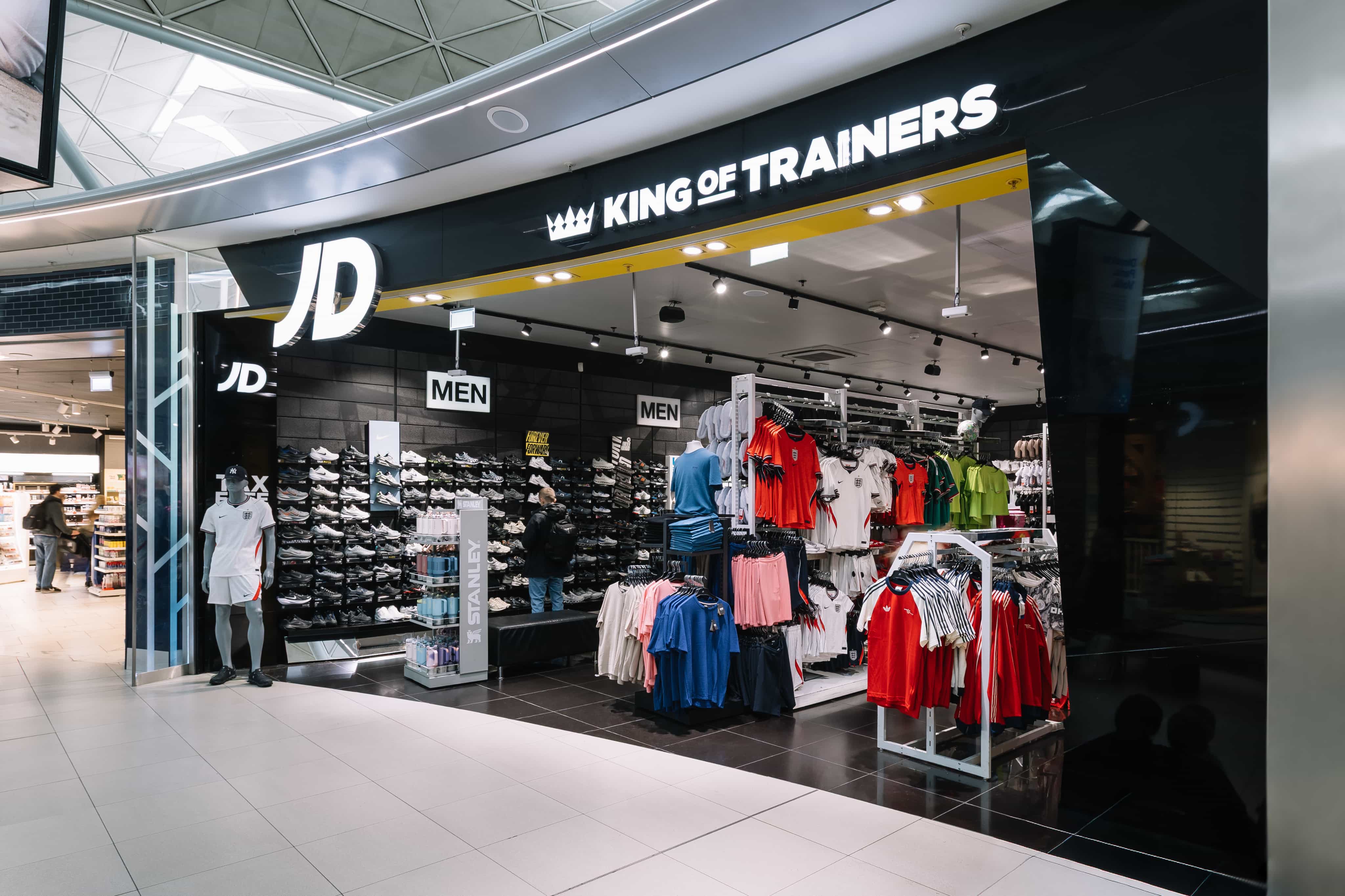 Sportswear store entrance featuring sneakers and colourful athletic apparel on display under a "KING OF TRAINERS" sign.