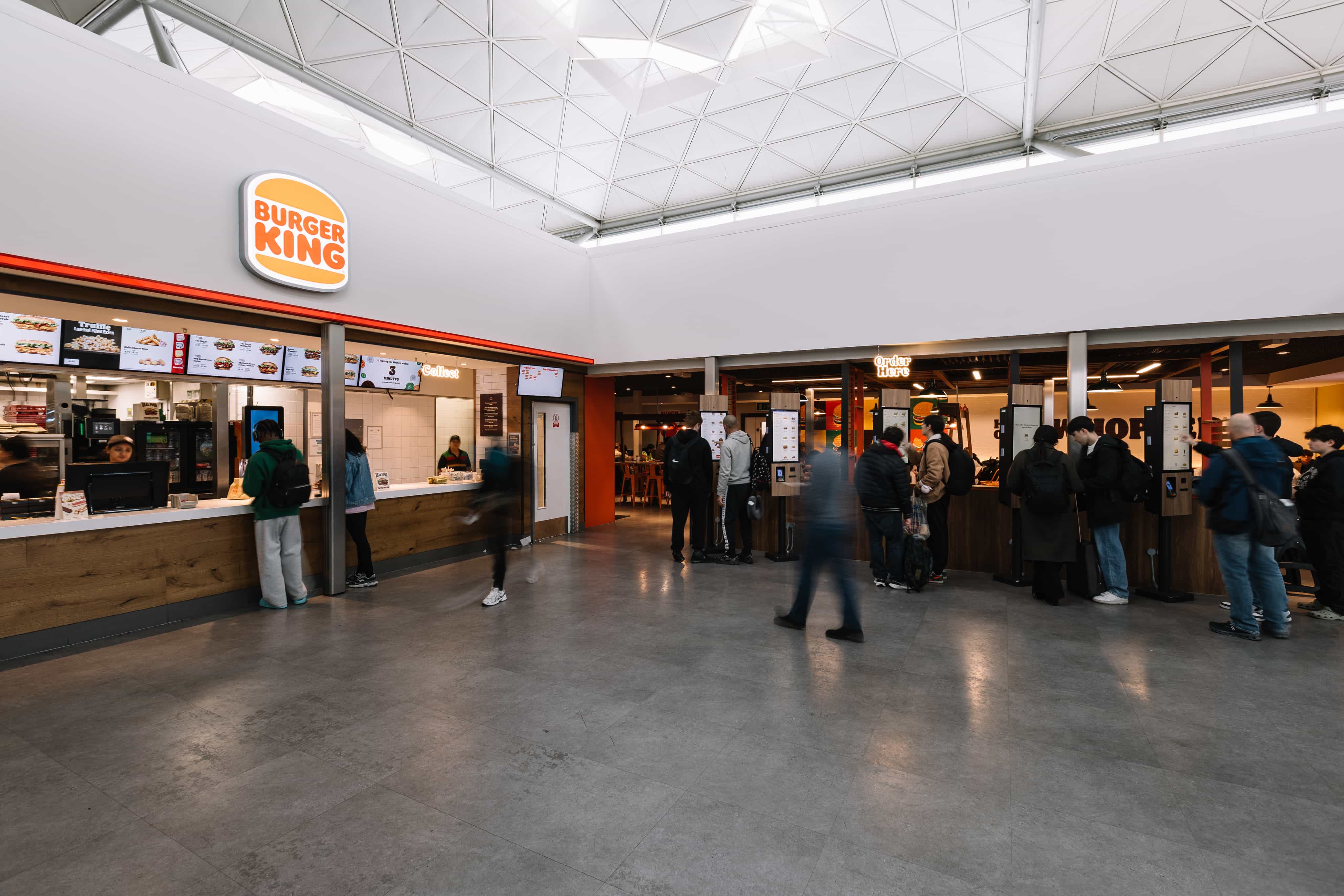 People ordering at a Burger King counter inside a modern, spacious food court.