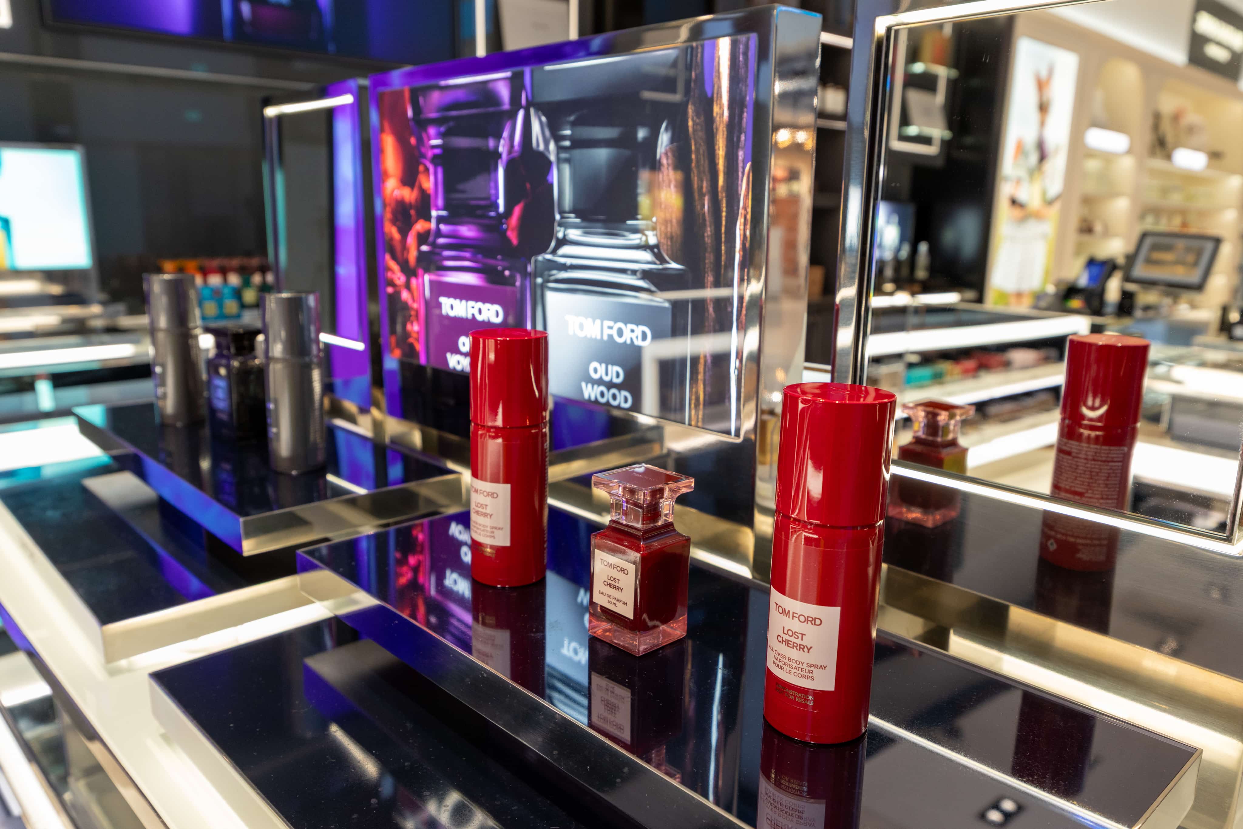 Tom Ford display in a store featuring various fragrances, including "Oud Wood" and "Lost Cherry," with sleek bottles on reflective surfaces.