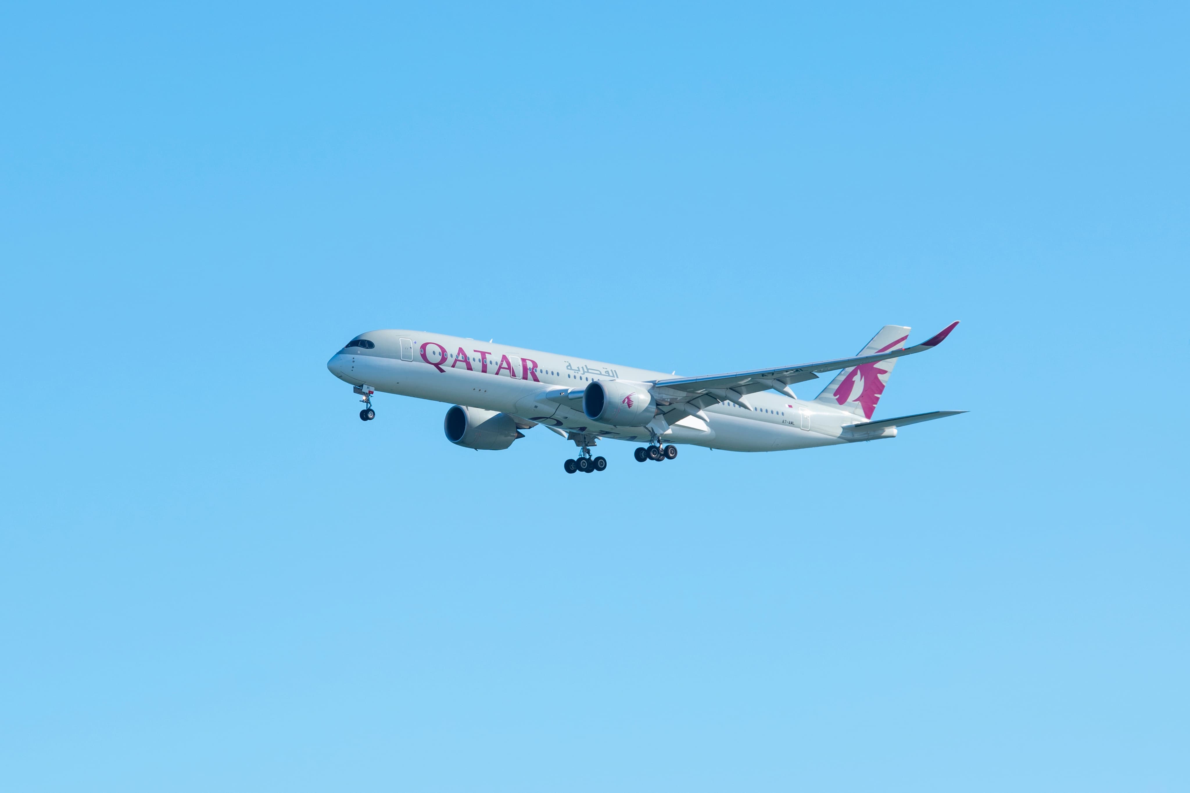 A Qatar Airways plane flying in a clear blue sky.