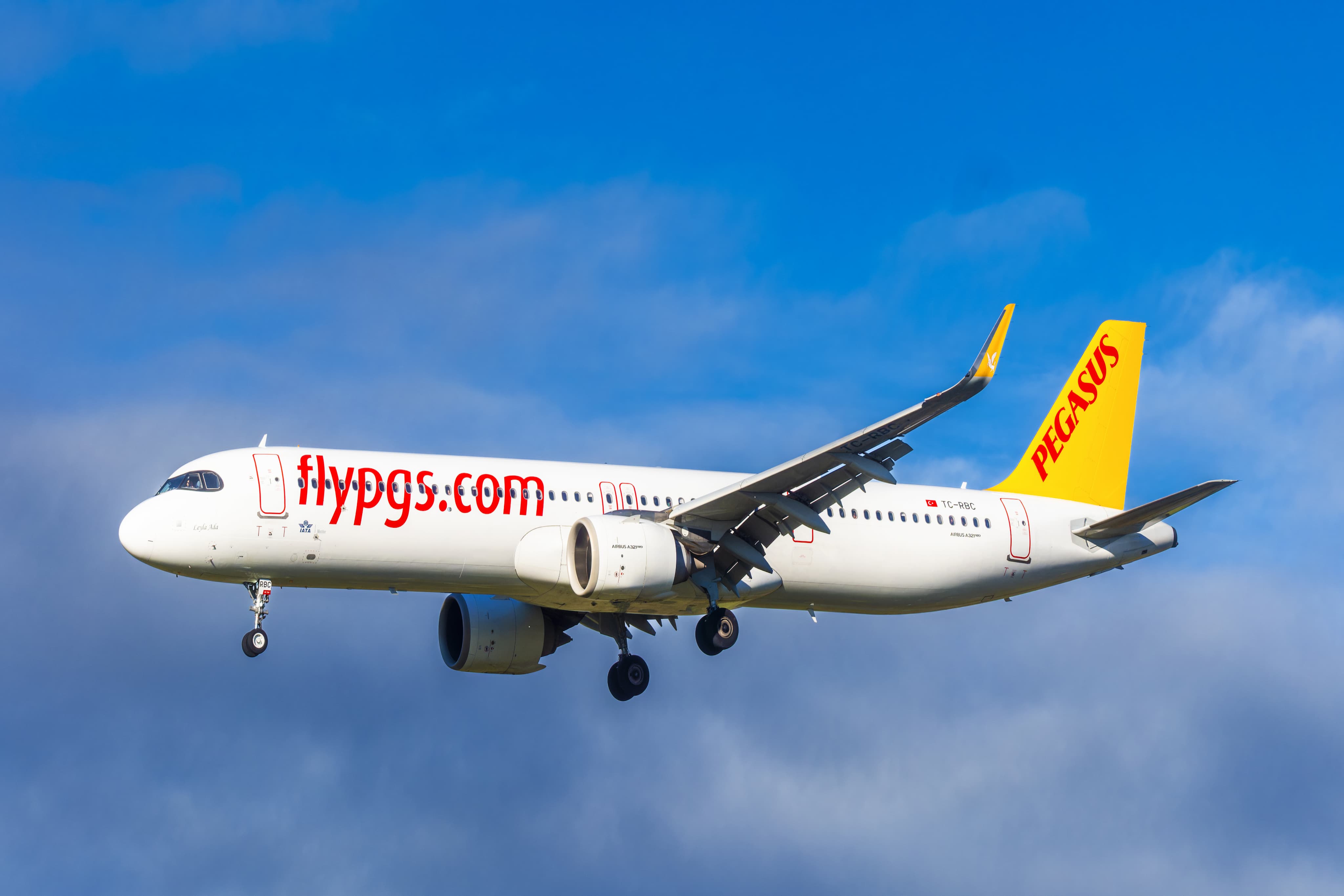 A Pegasus Airlines plane in flight against a blue sky, with "flypgs.com" on the fuselage and a yellow tail fin.
