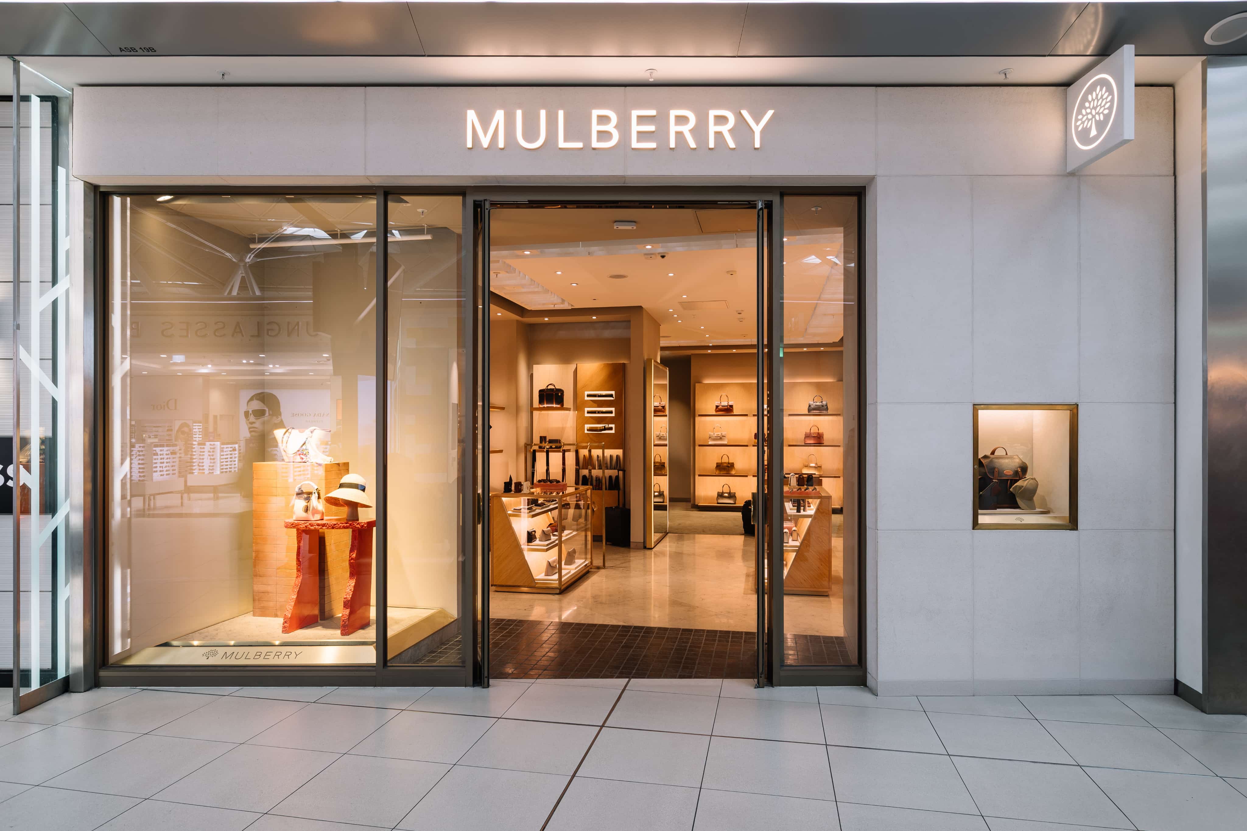Storefront of Mulberry, showcasing luxury bags and accessories through glass doors and display windows with elegant interior lighting.