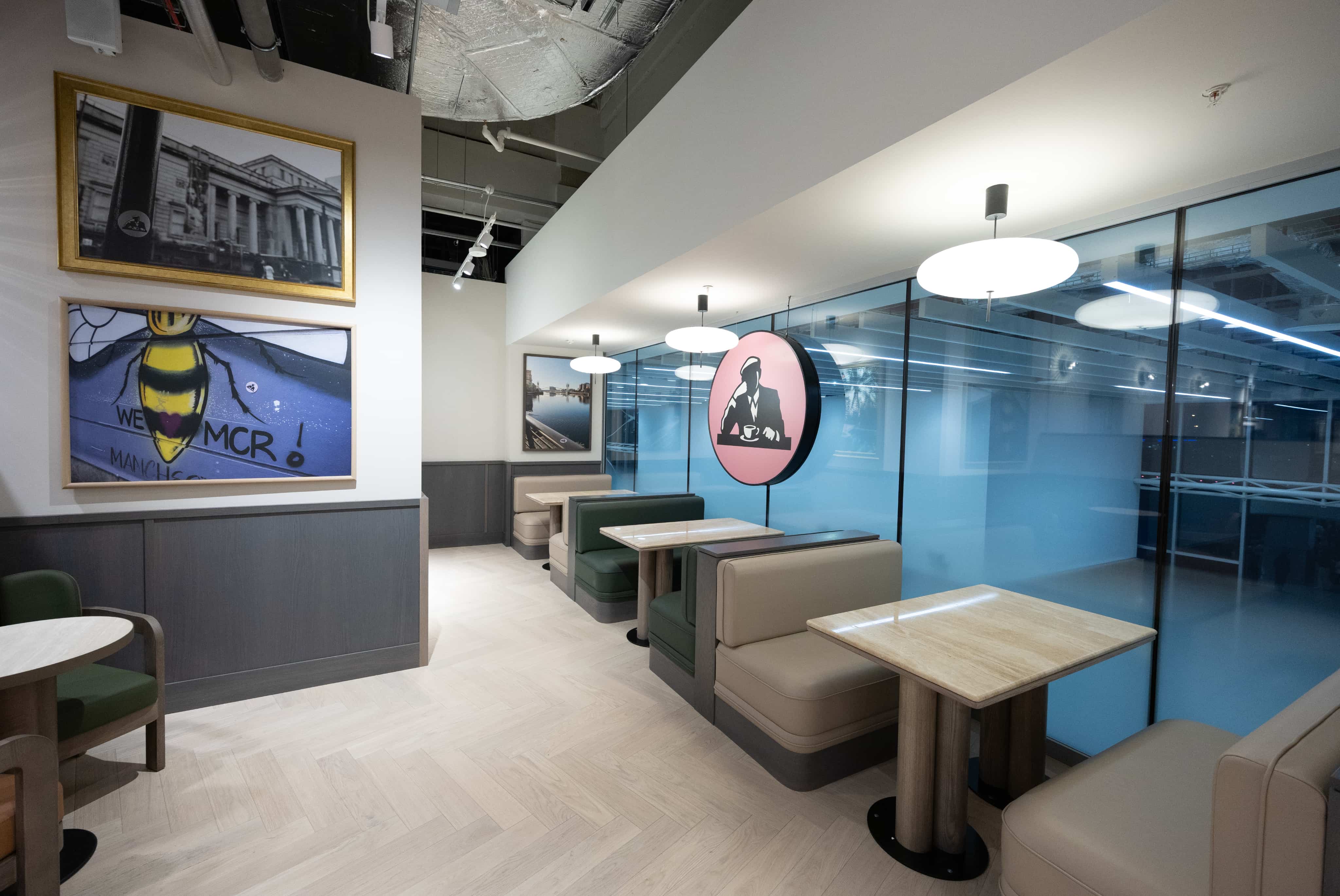 Modern cafe interior with booth seating, large artworks on walls, and overhead pendant lights, against a backdrop of frosted glass panels.