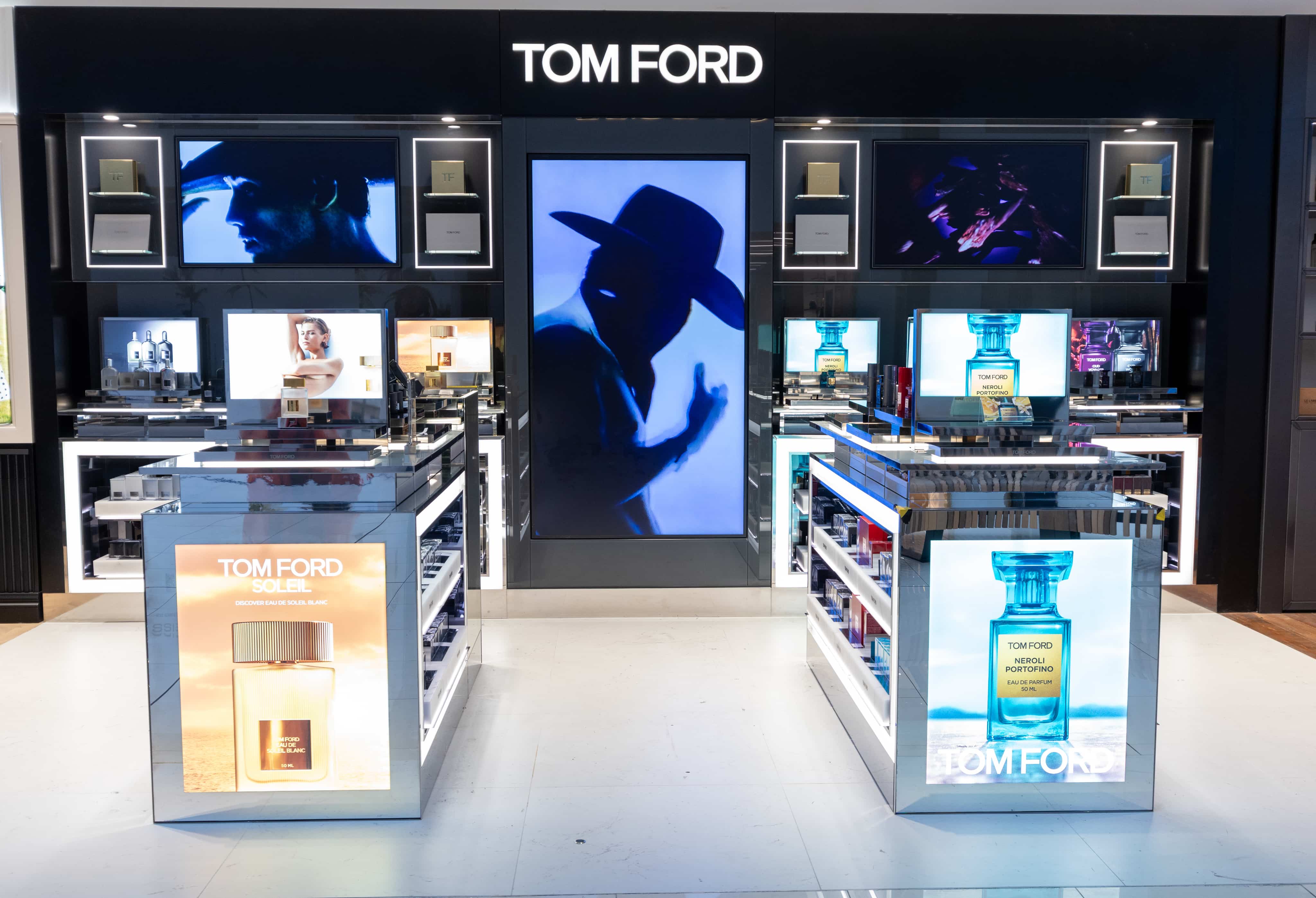 Tom Ford store display featuring large digital screens, perfume products, and branded visuals, including images of bottles and a silhouette.