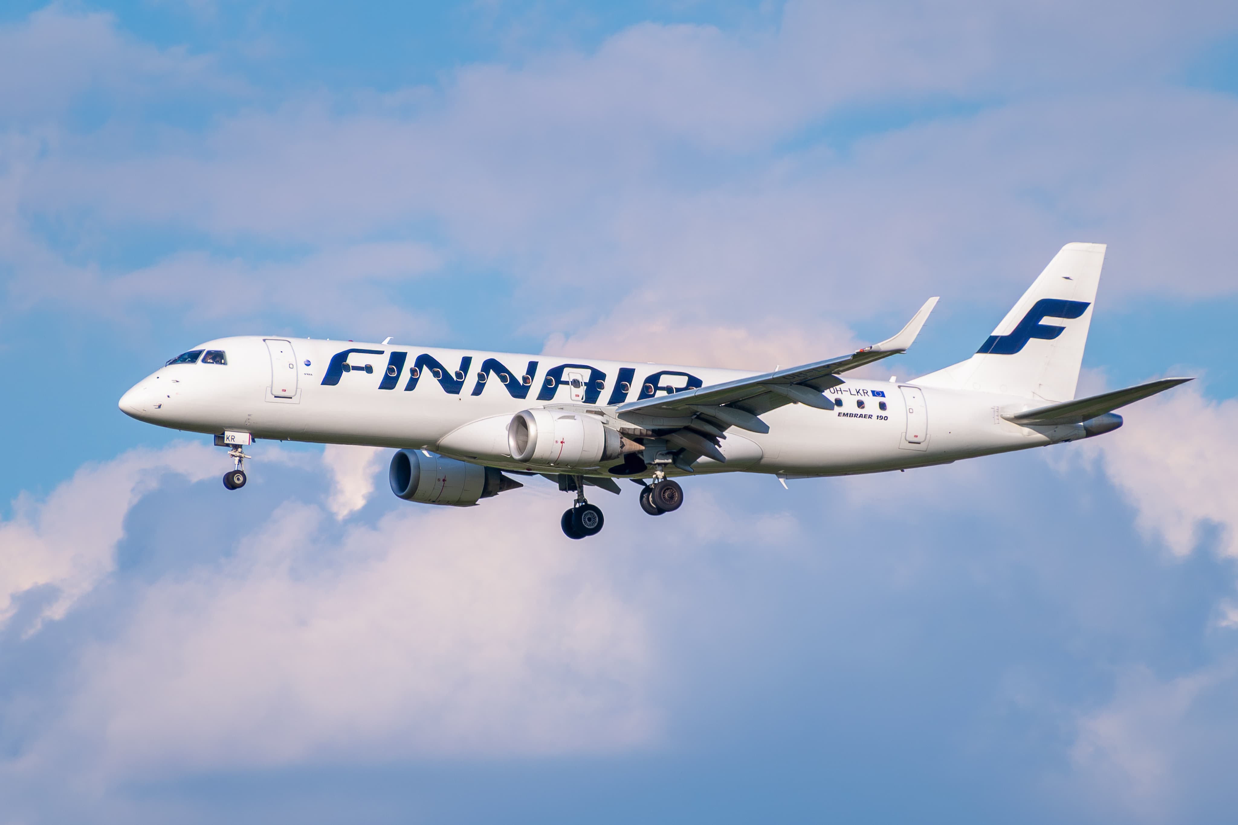A Finnair Embraer 190 airplane in flight with landing gear down against a blue sky with clouds.