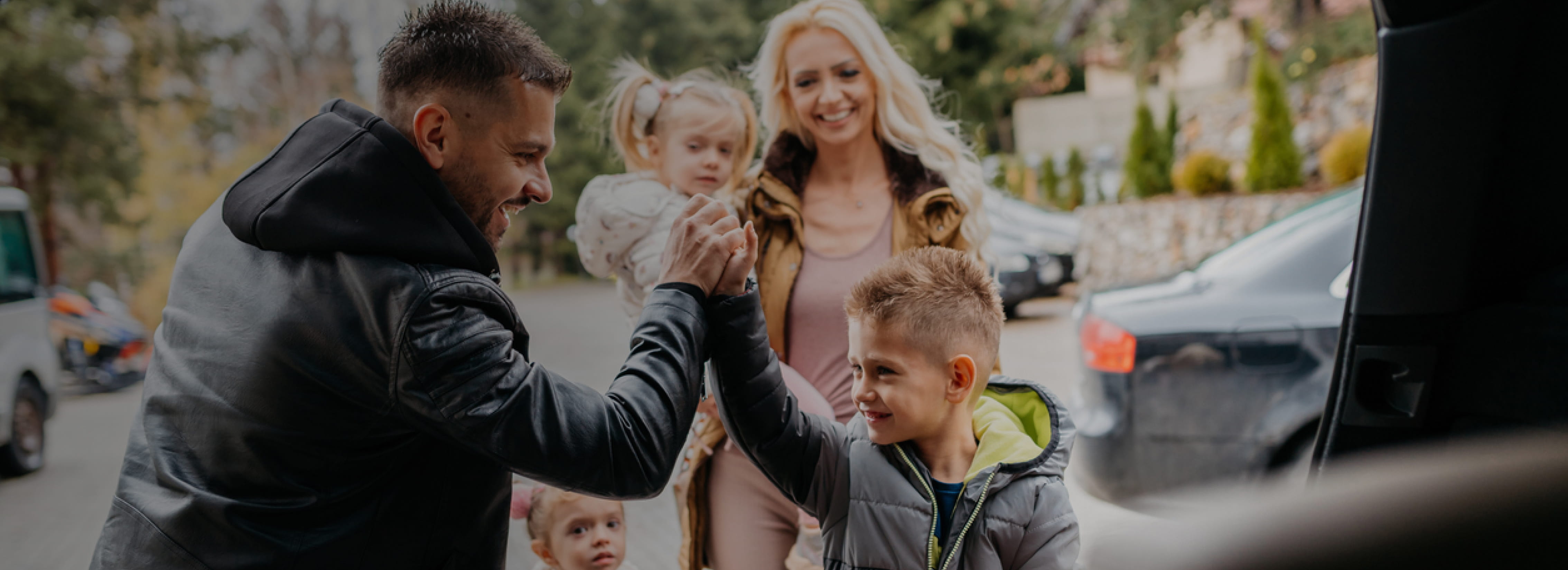 Image of family in boot of car with father and son high fiving