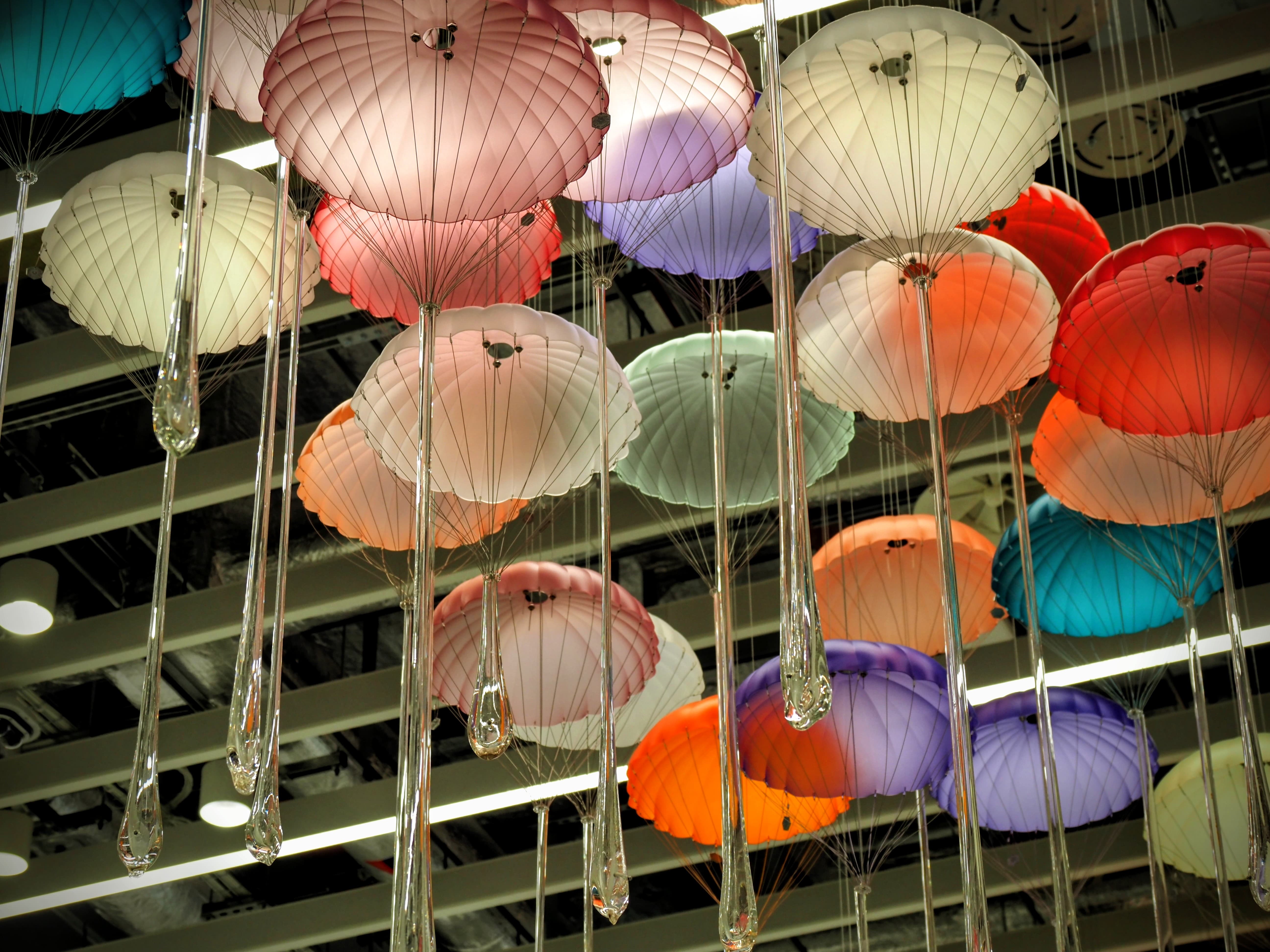 Colourful umbrella-like art installation hanging from the ceiling with glass teardrops in a modern setting.